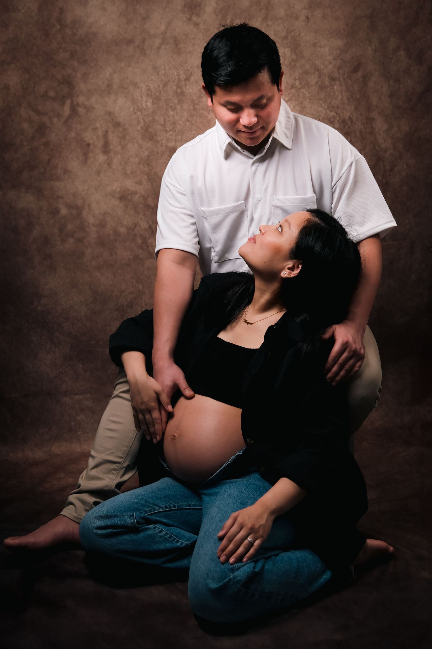 Intimate maternity portrait session showing couple's connection against brown backdrop.