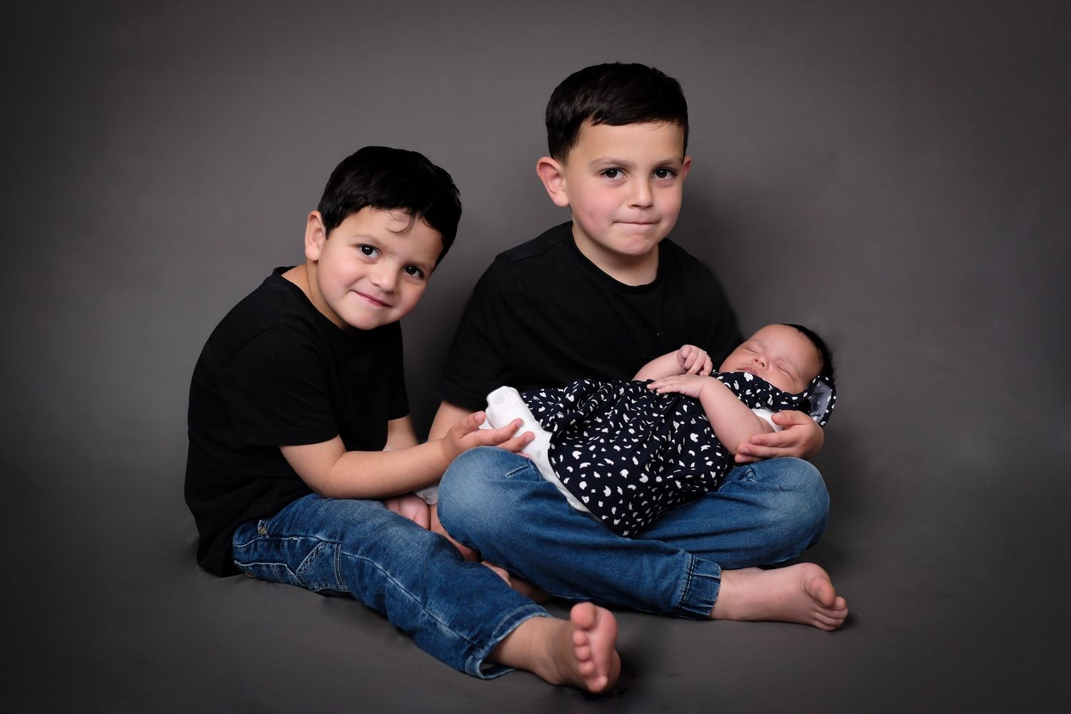 Studio portrait showing tender family moment against dark grey background.