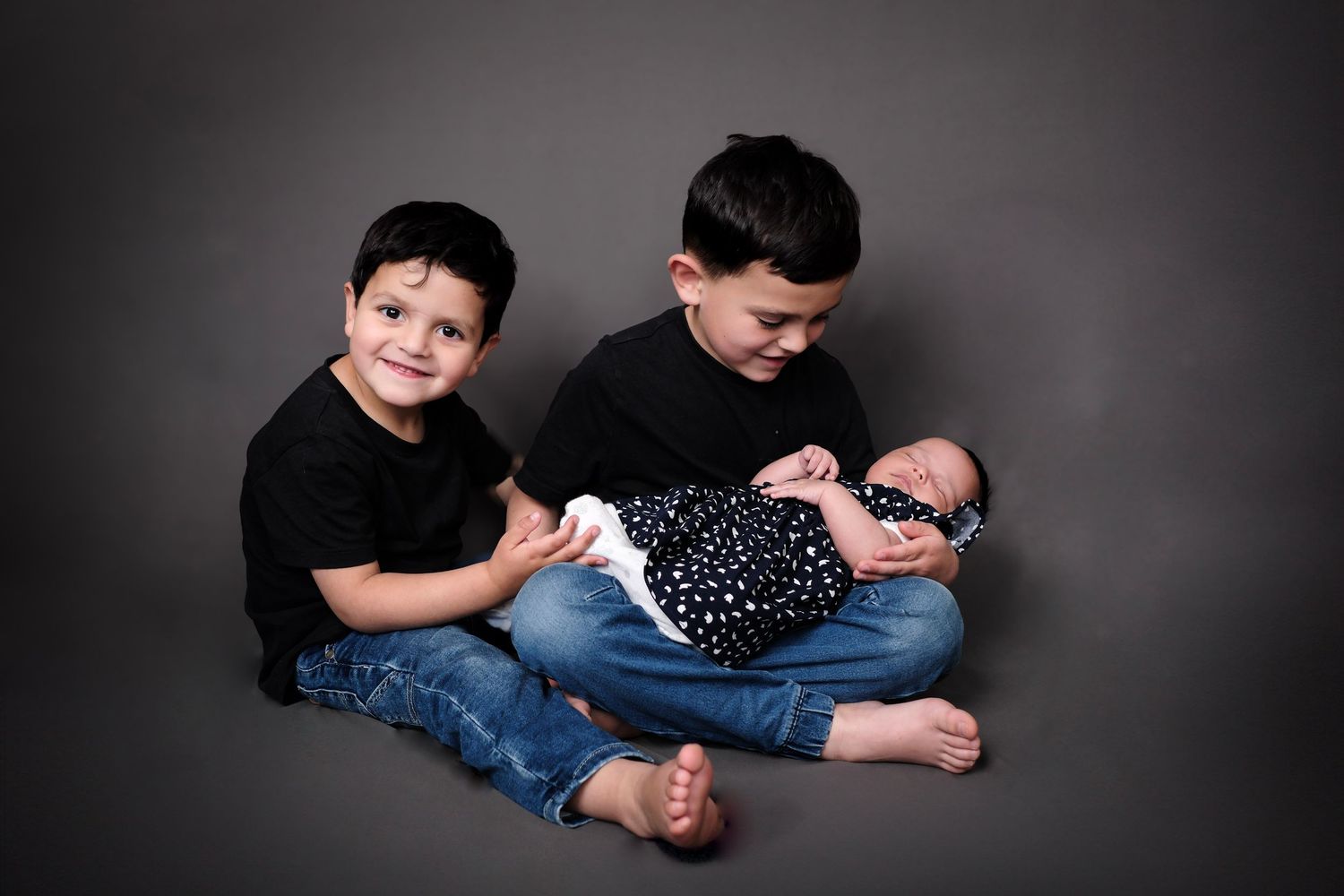 Family portrait with siblings and baby in black and white against dark background.
