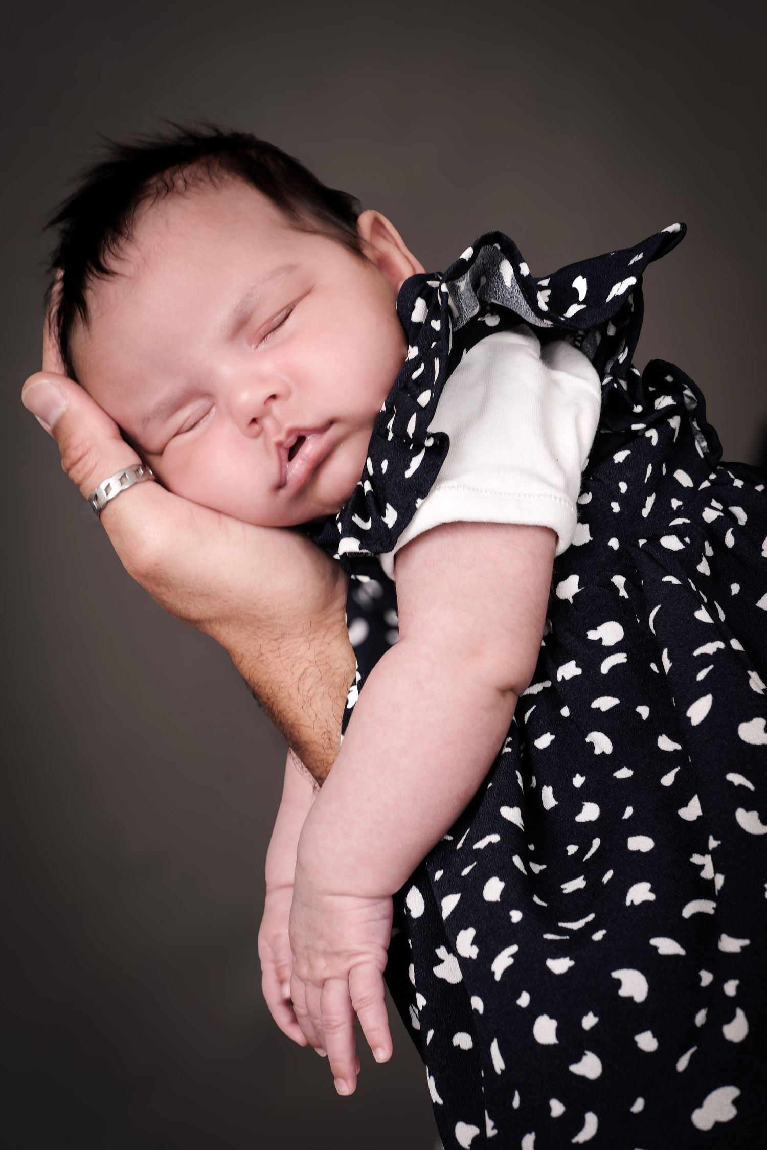 Sleeping infant wearing polka dot outfit in dramatic black and white portrait series.