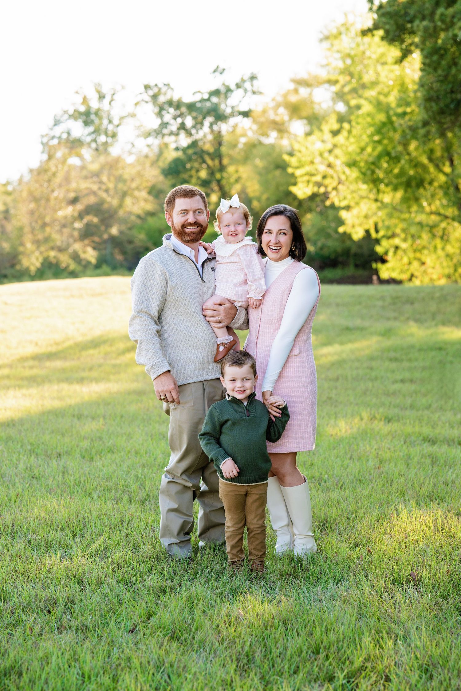 Smiling family of four poses in green park at golden hour in coordinated fall outfits.