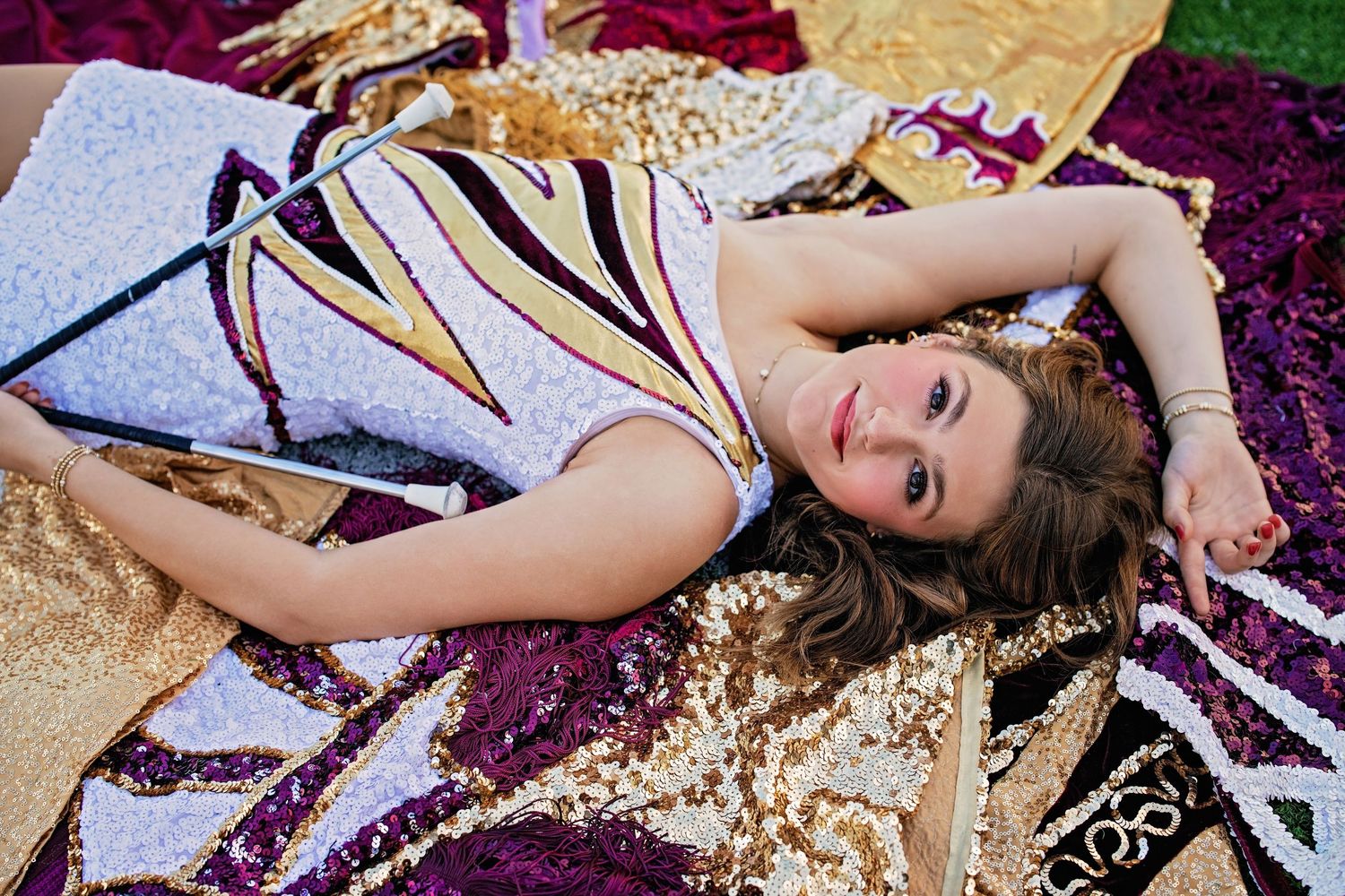 Young woman in colorful dress lying on sequined blankets outdoors, smiling up at camera.