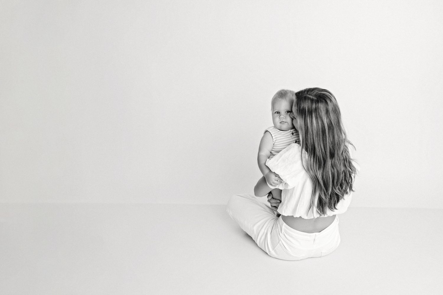 Mother sitting cross-legged holding baby in black and white portrait photo.