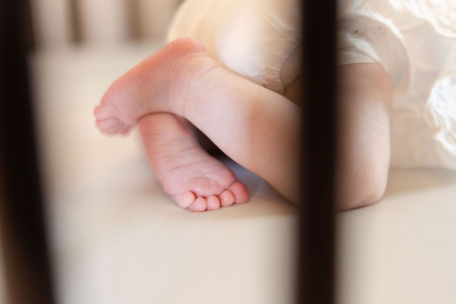 Close-up of newborn baby tiny feet resting in wooden crib slats.