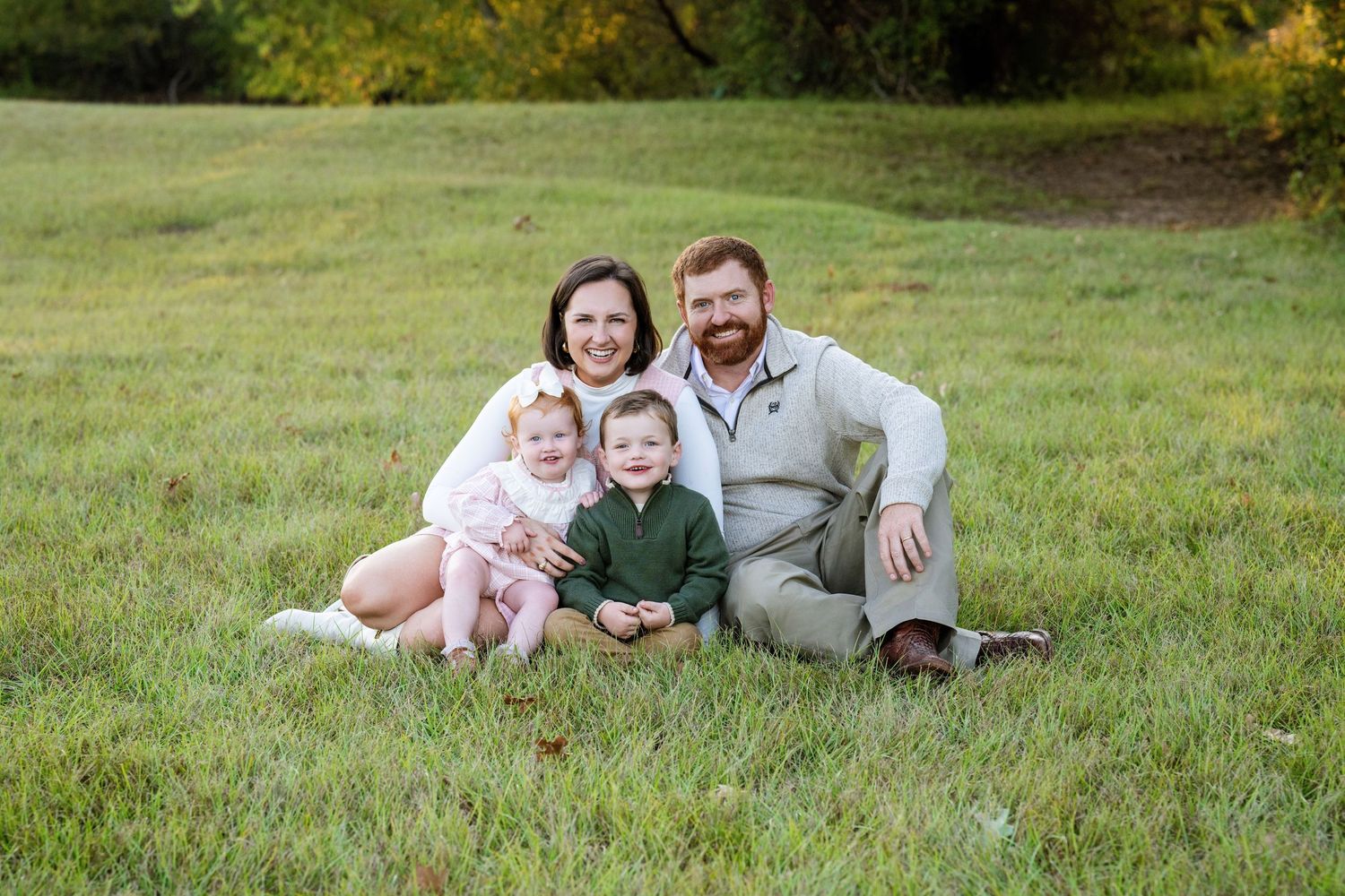 Happy family of four poses on lush green grass for an outdoor portrait session in autumn.