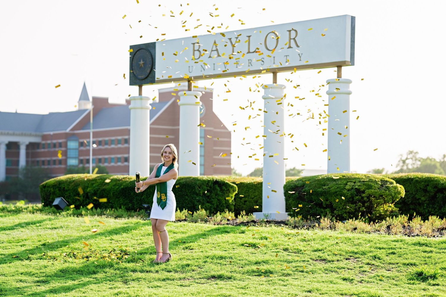 Graduate celebrates with confetti in front of Baylor University sign outdoors.