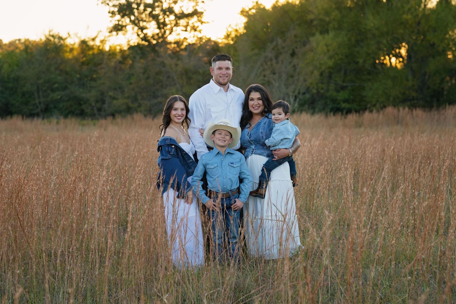 Family of five posing in a golden field at sunset, dressed in western-style outfits.