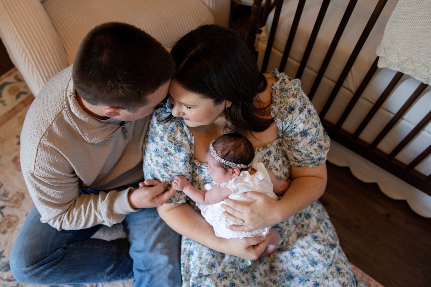 New parents leaning over newborn baby in wooden nursery crib together.
