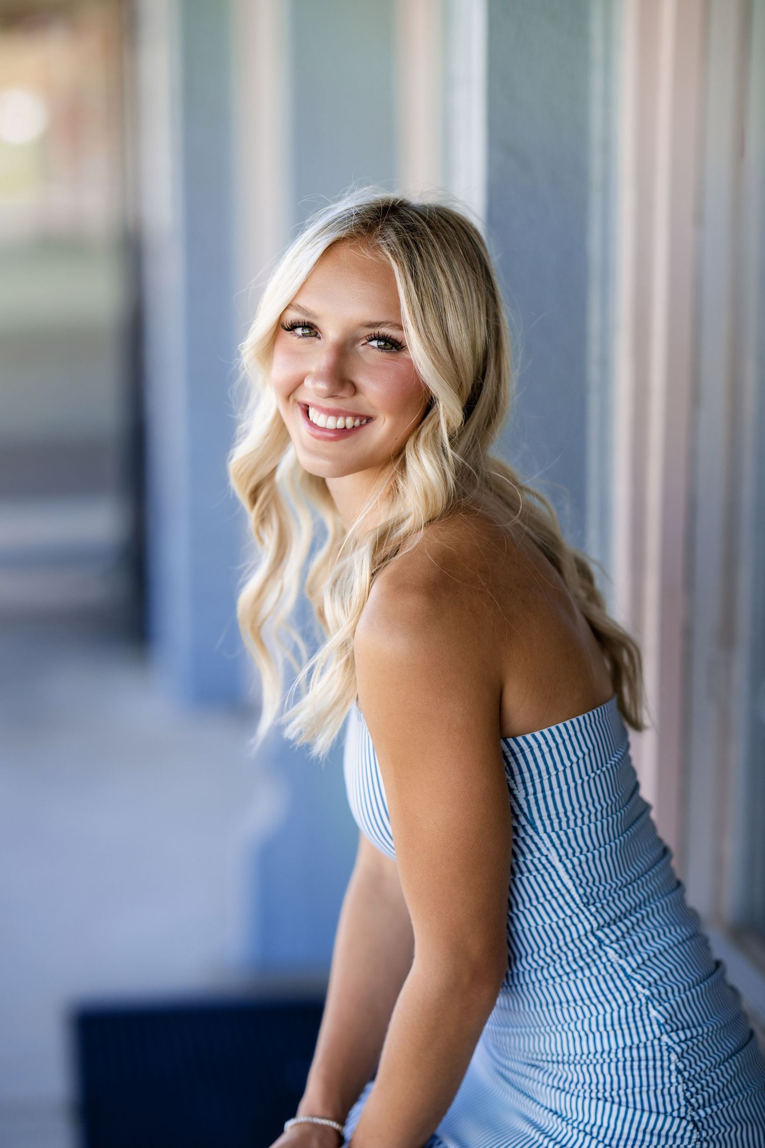 Smiling blonde teen in blue striped strapless dress poses for senior portrait outdoors.