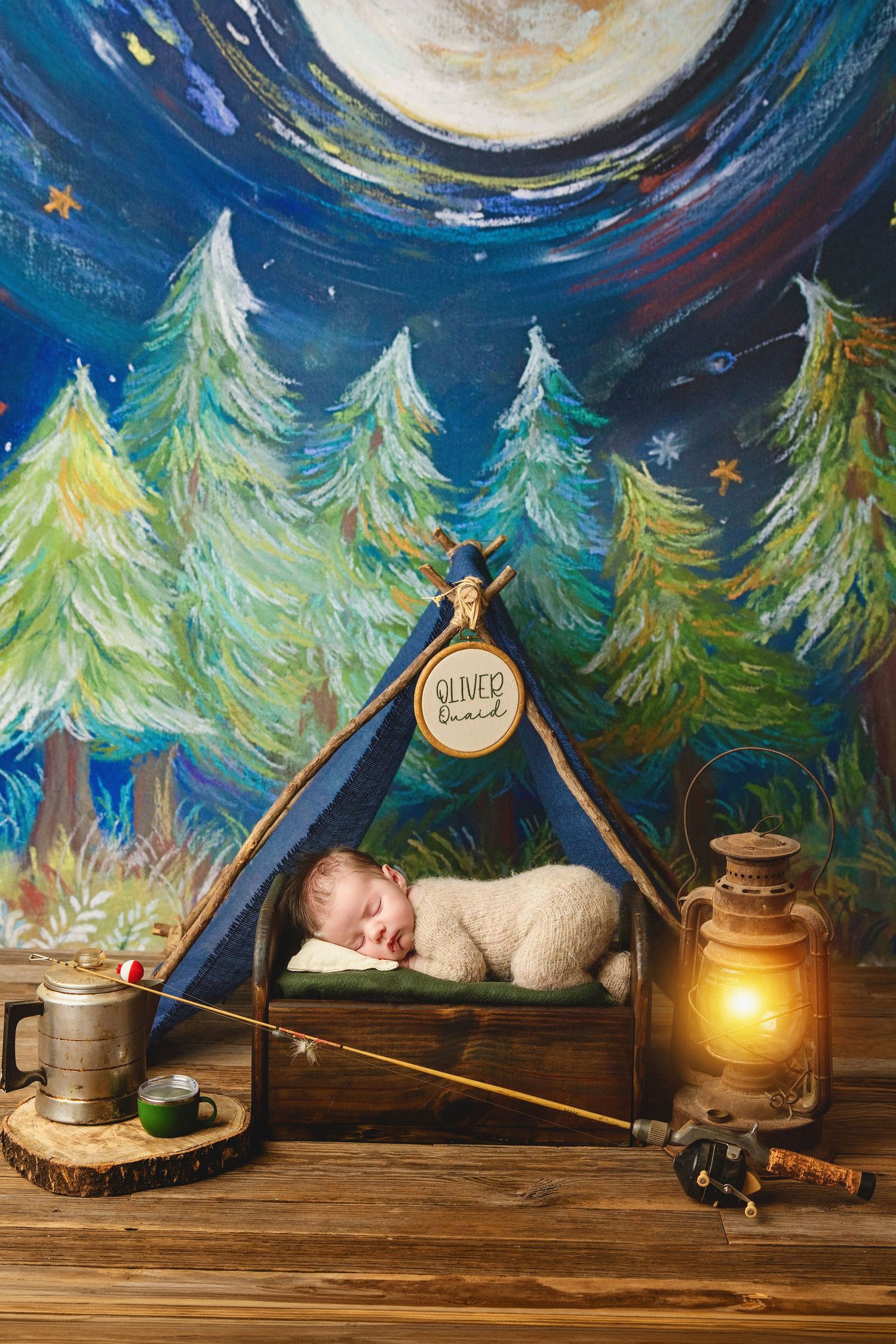 Newborn baby sleeps peacefully in a camping-themed photography setup with tent and lantern backdrop.