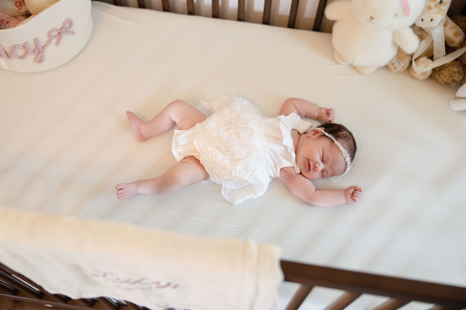 Overhead view of newborn baby in white romper lying in wooden crib.