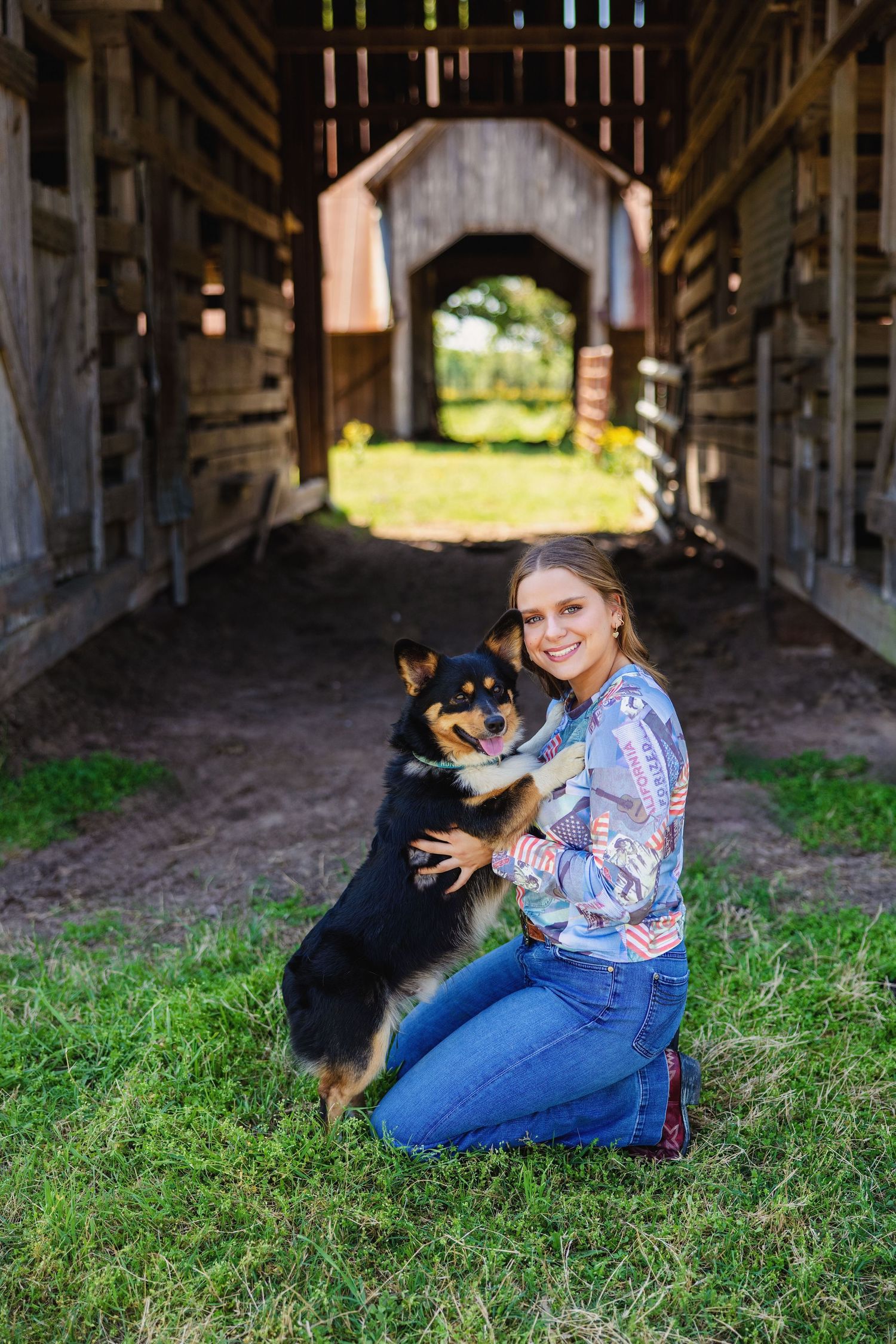 Smiling young woman kneeling with black and tan dog inside wooden covered bridge barn.