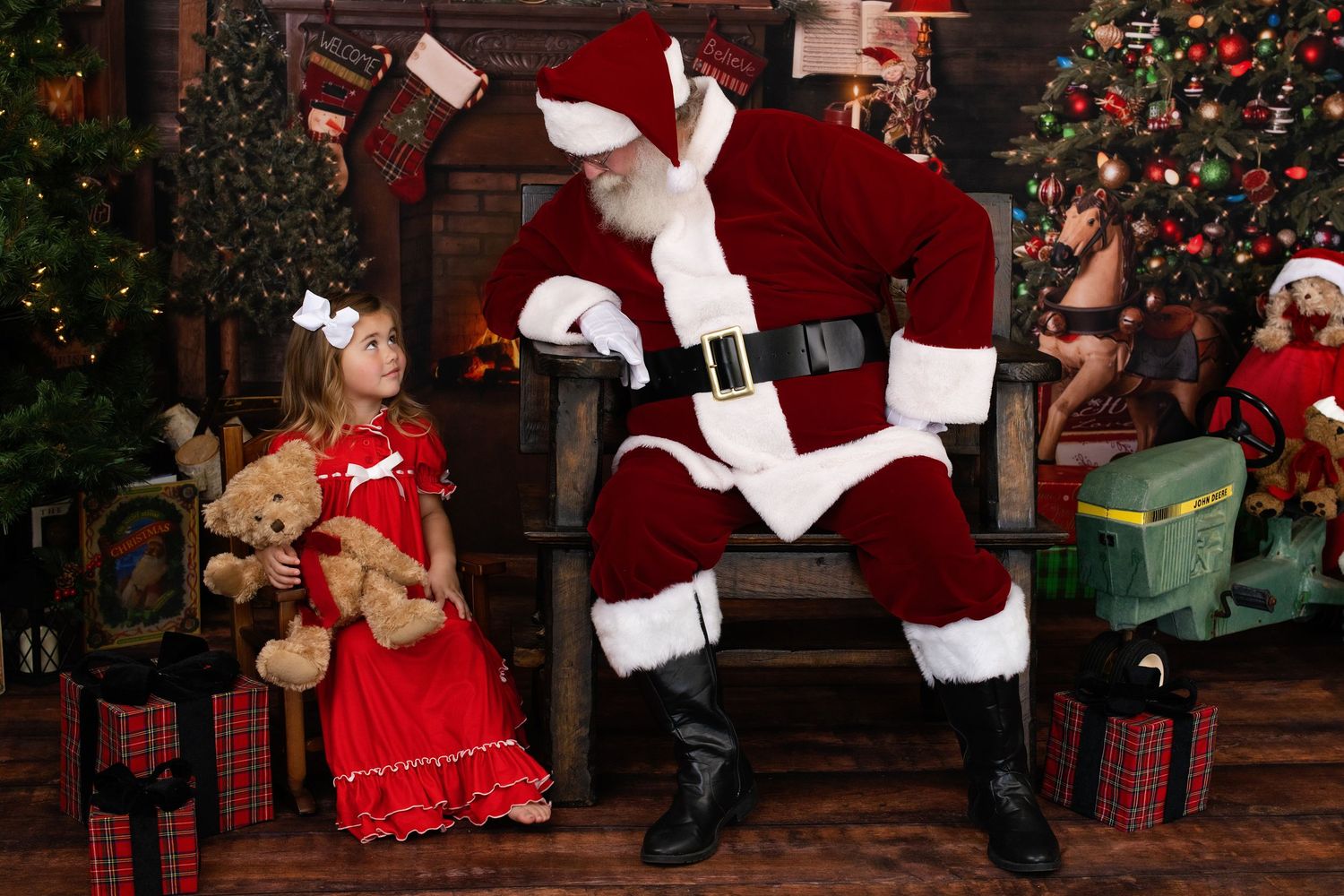Young girl in red dress meeting Santa Claus surrounded by Christmas decorations and gifts.