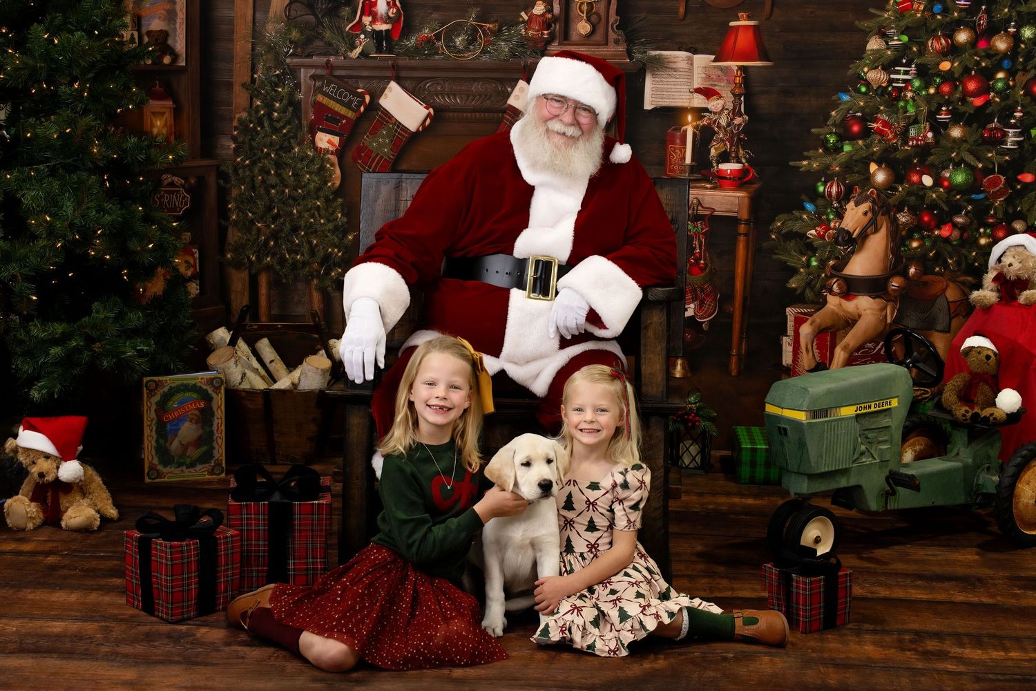 Two young girls sitting with a puppy in front of Santa Claus in a festive Christmas setting.