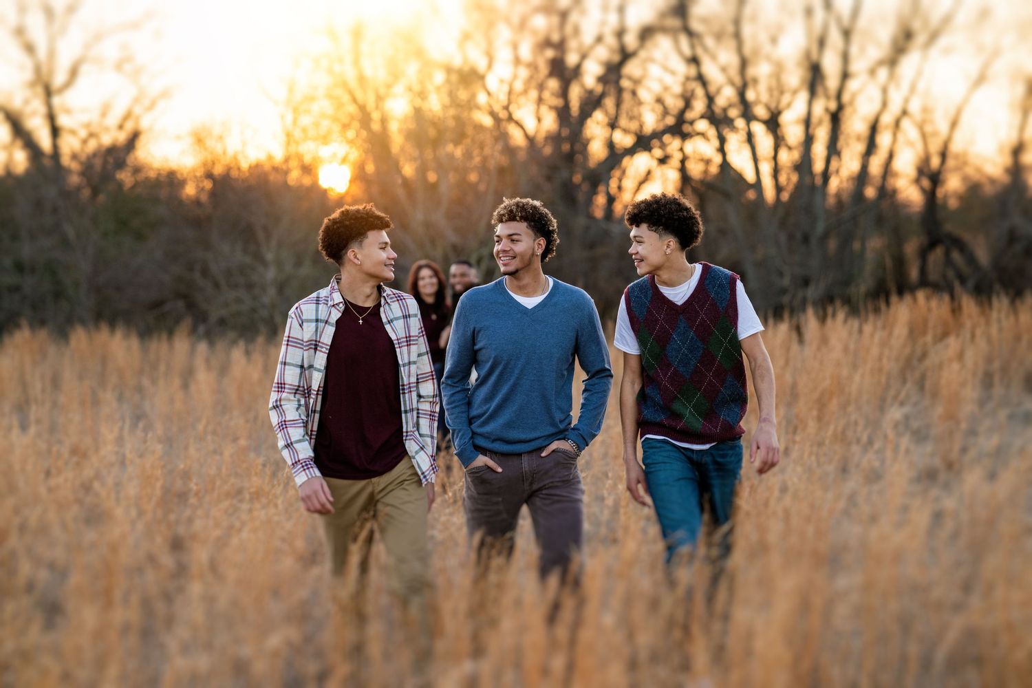 Three teenage boys walk through golden field at sunset in casual outdoor portrait session.