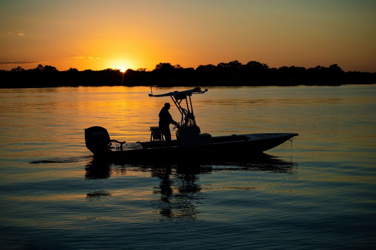 Silhouette of a fisherman on a boat against a stunning golden sunset over calm water.