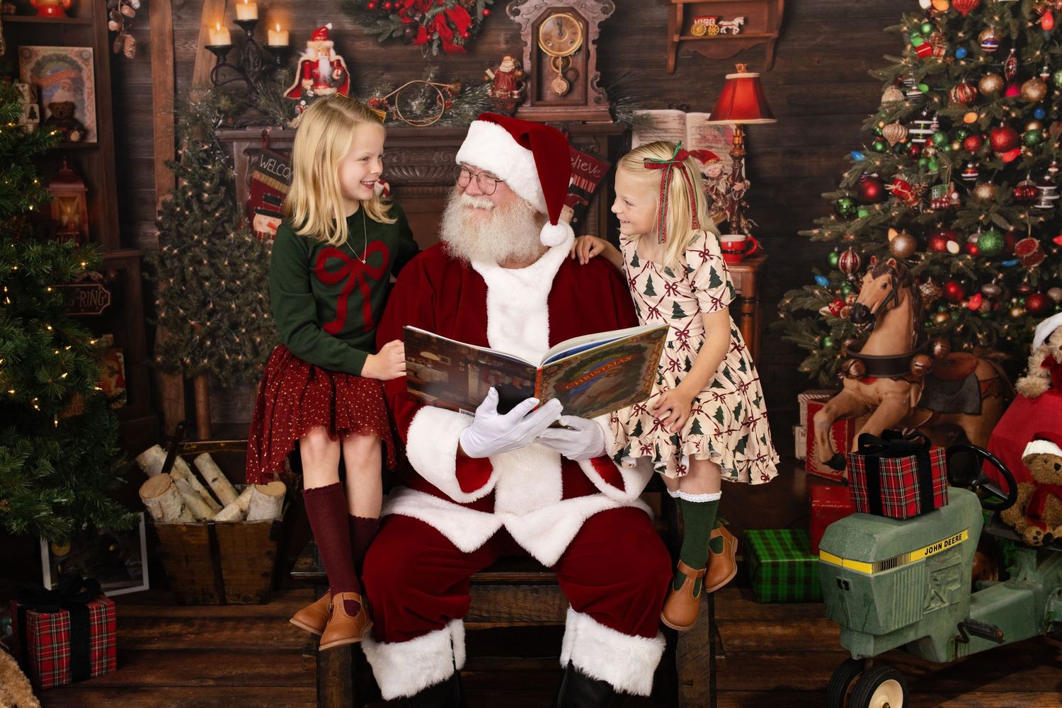 Santa Claus reading a storybook to two delighted young girls in a decorated holiday setting.