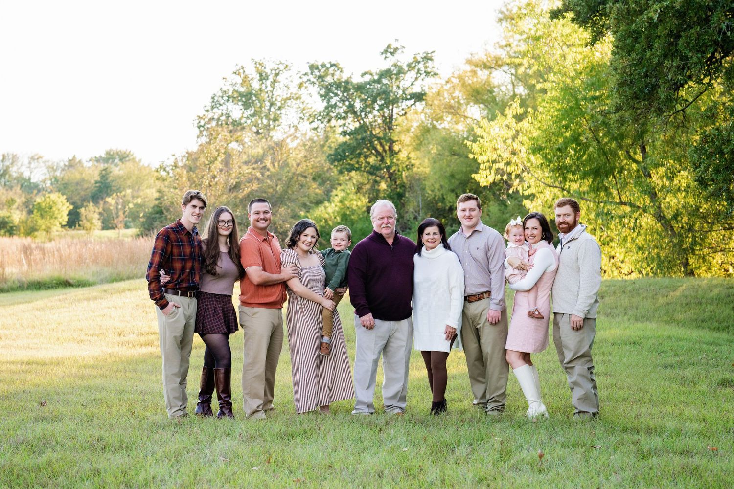 Extended family of nine adults posing together on a green lawn with lush trees.