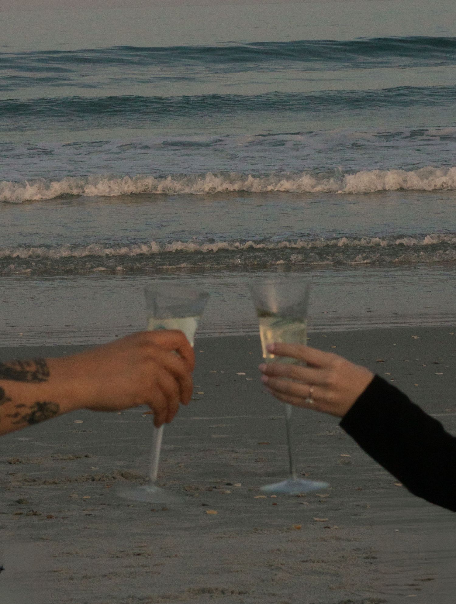 Champagne glasses with waves during a natural engagement photography session in Wrightsville Beach, NC.