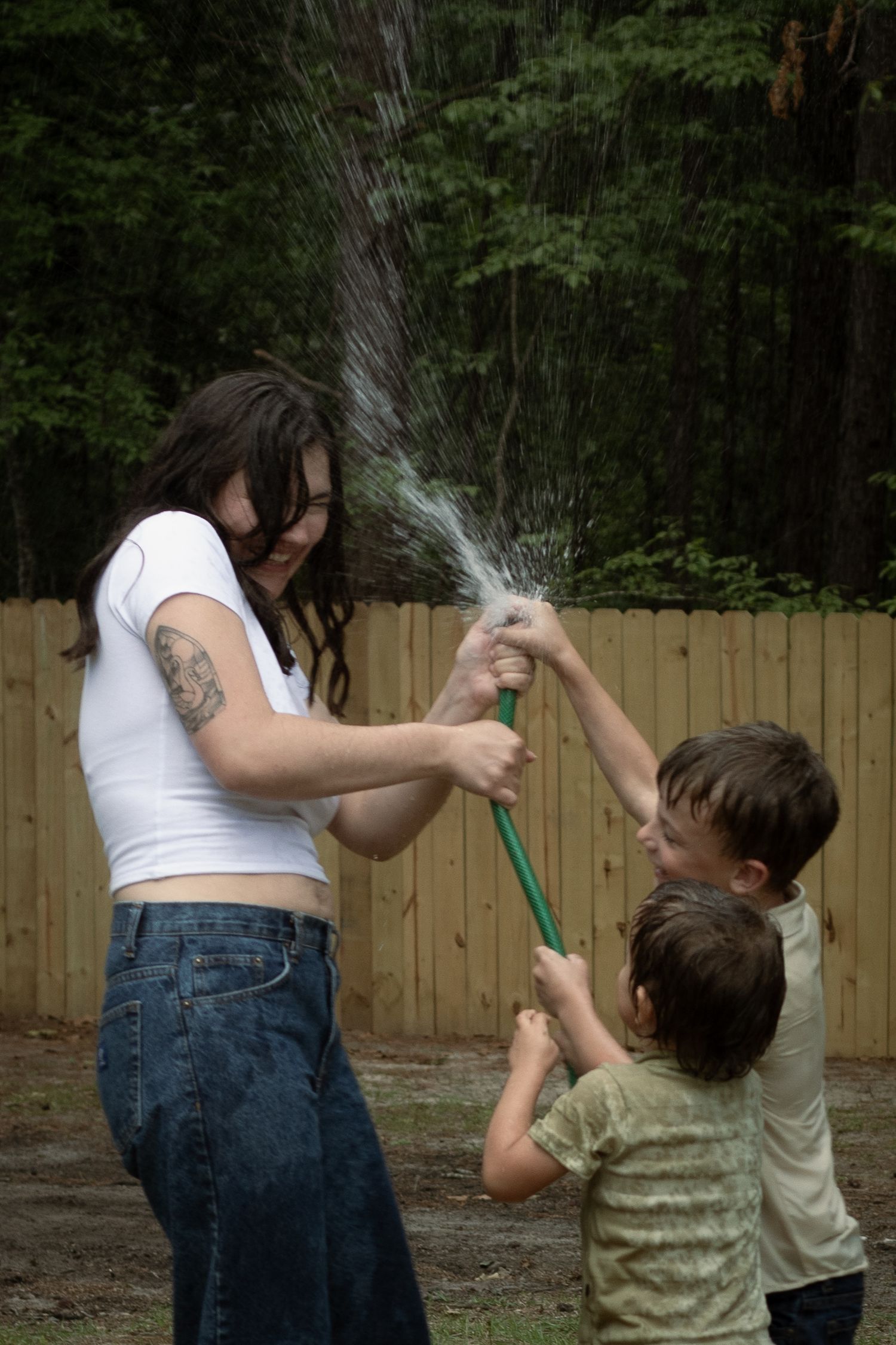 Family laughing and spraying each other with a garden hose during a playful family photography session in Raeford, NC.