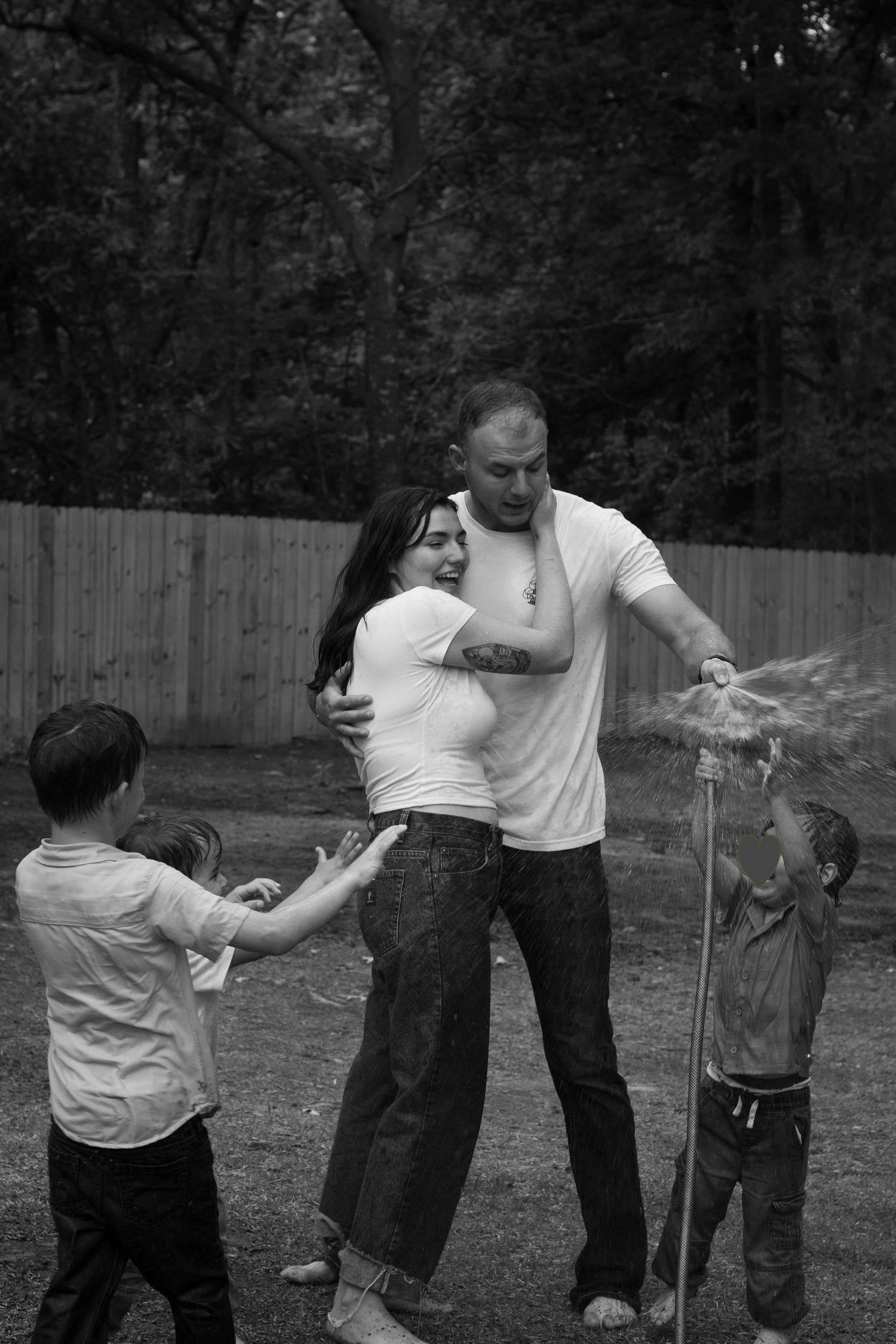 Family laughing and spraying each other with a garden hose during a playful family photography session in Raeford, NC.