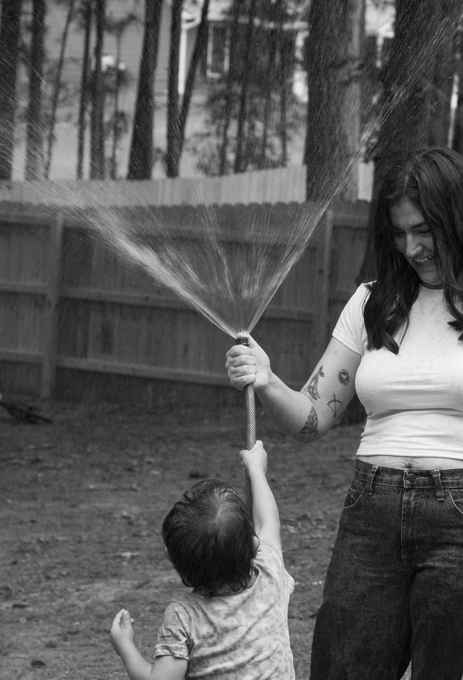 Family laughing and spraying each other with a garden hose during a playful family photography session in Raeford, NC.
