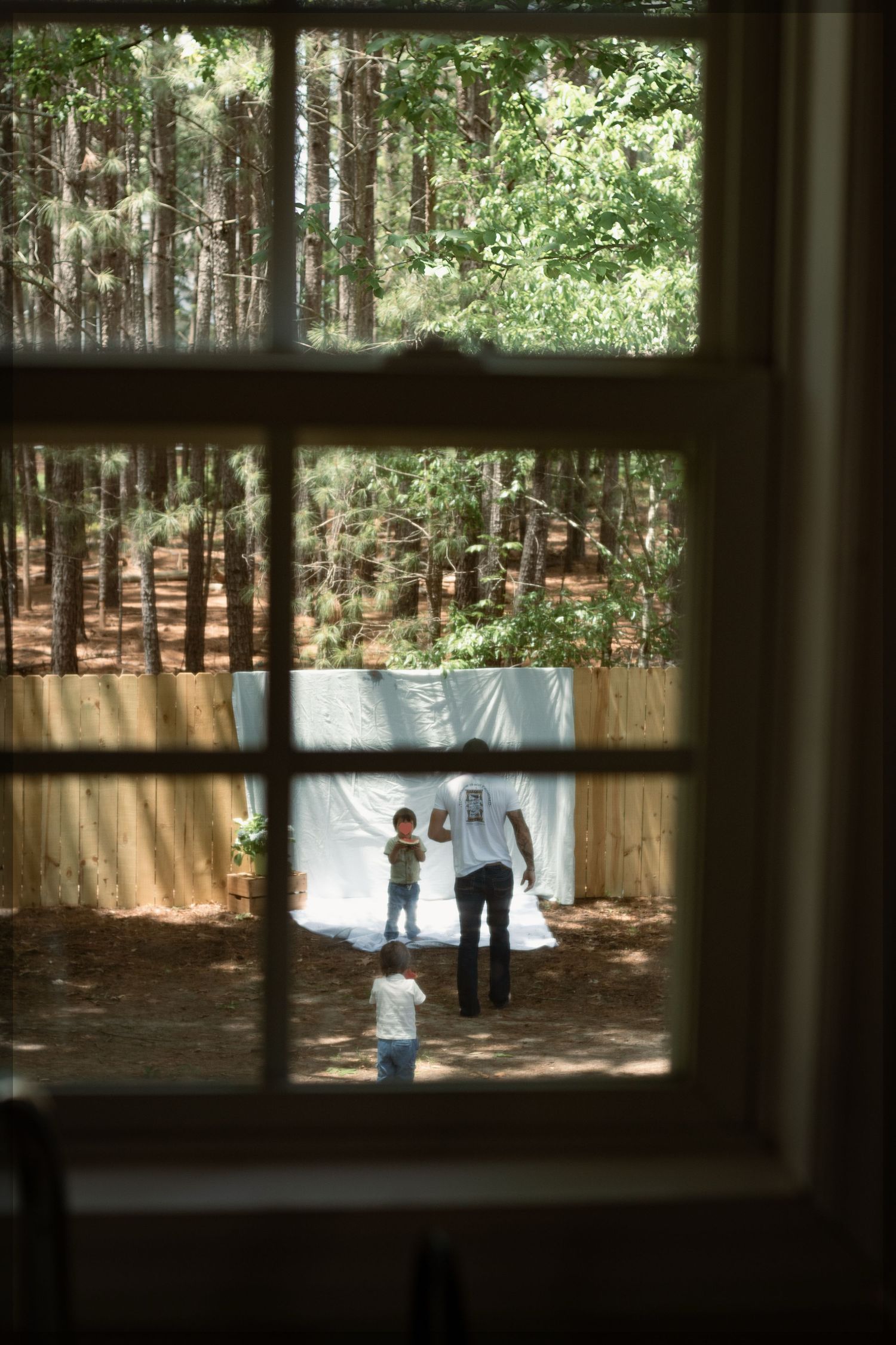 Photo through window of family eating watermelon during a playful family photography session in Raeford, NC.