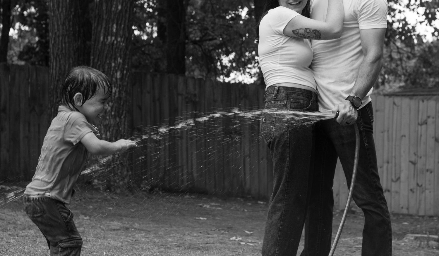 Family laughing and spraying each other with a garden hose during a playful family photography session in Raeford, NC.