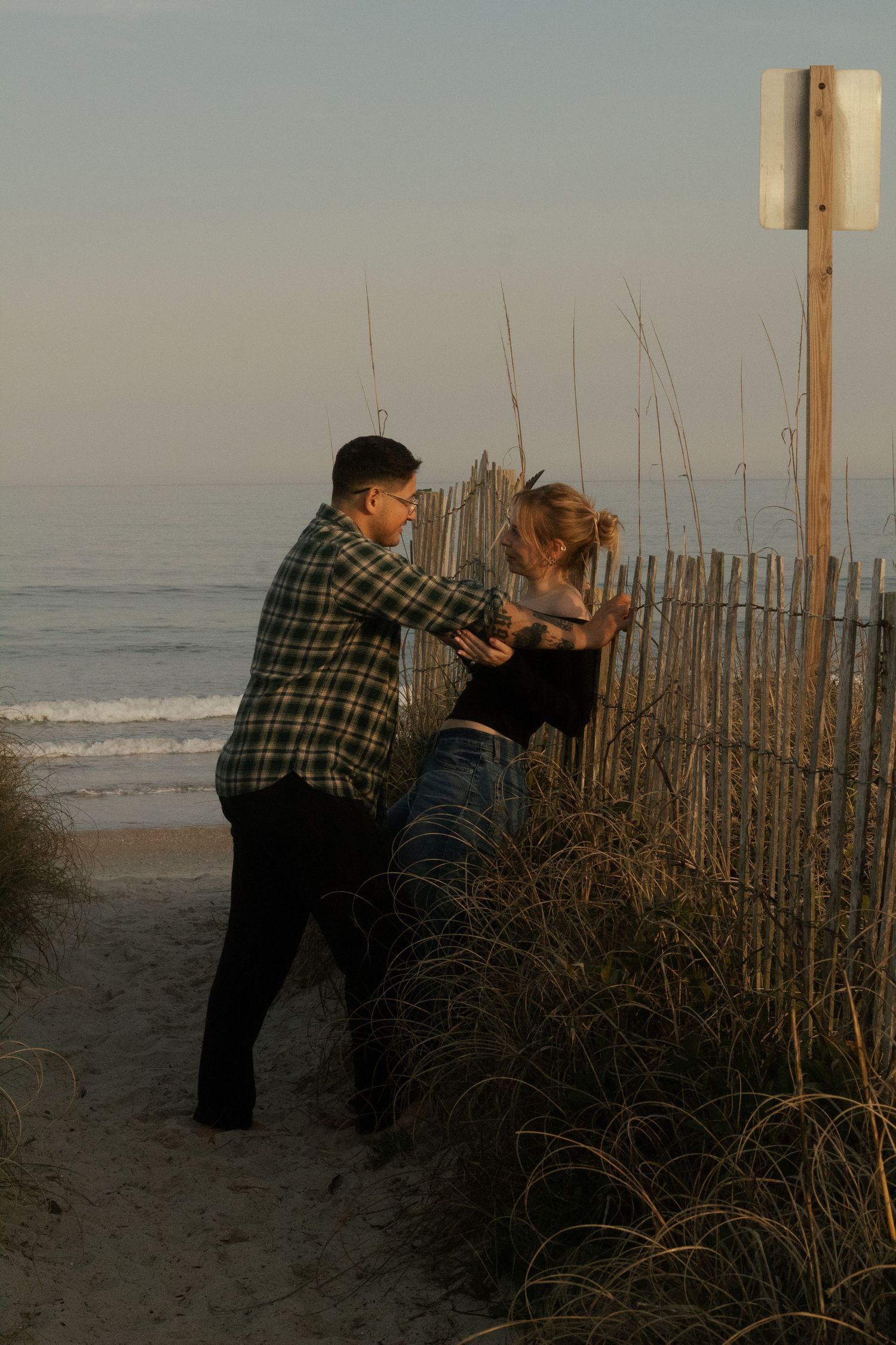 Engaged couple leaning against a beach fence during an engagement photography session in Wrightsville Beach, NC.