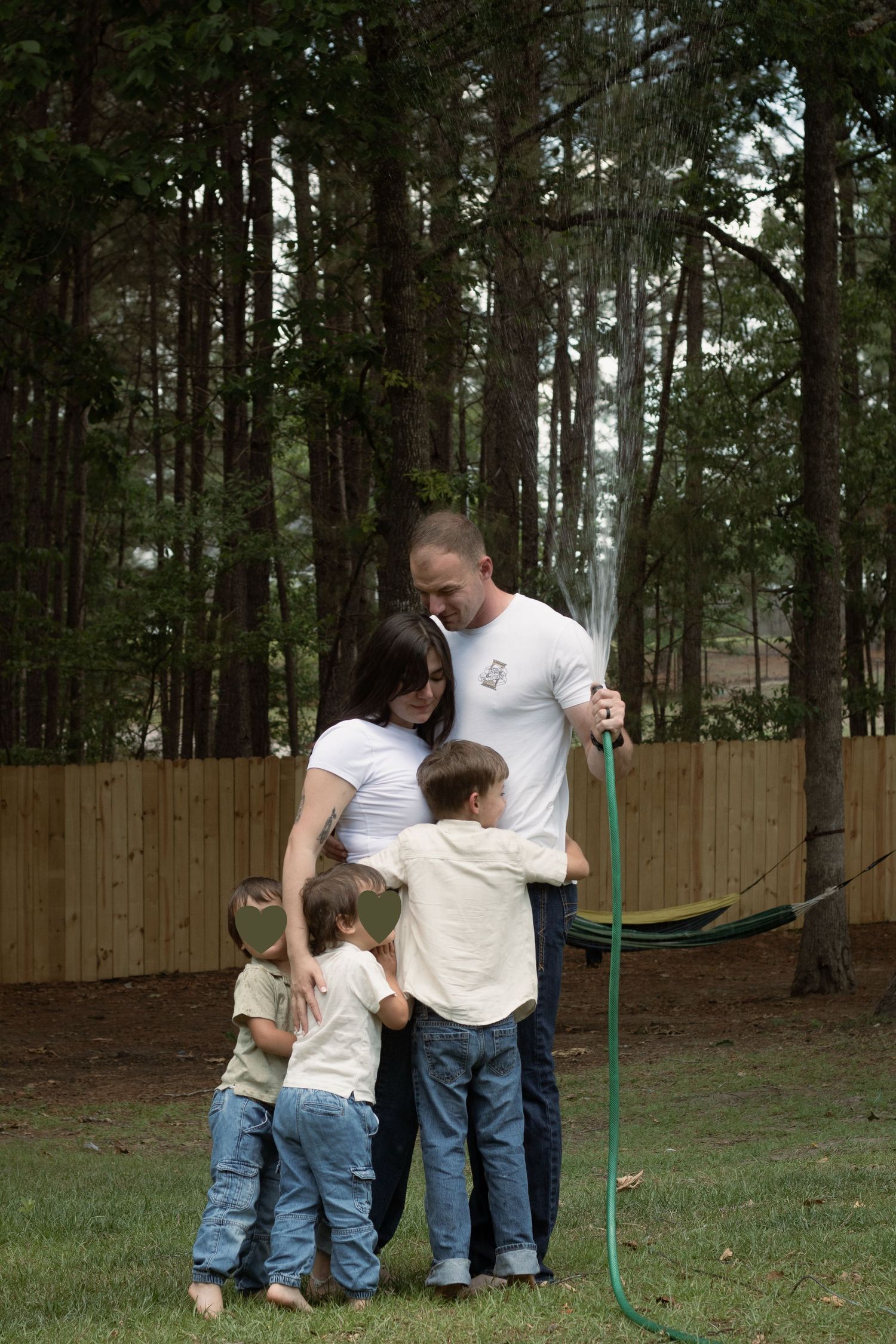 Family hugging under spray of garden hose held by dad during a playful family photography session in Raeford, NC.