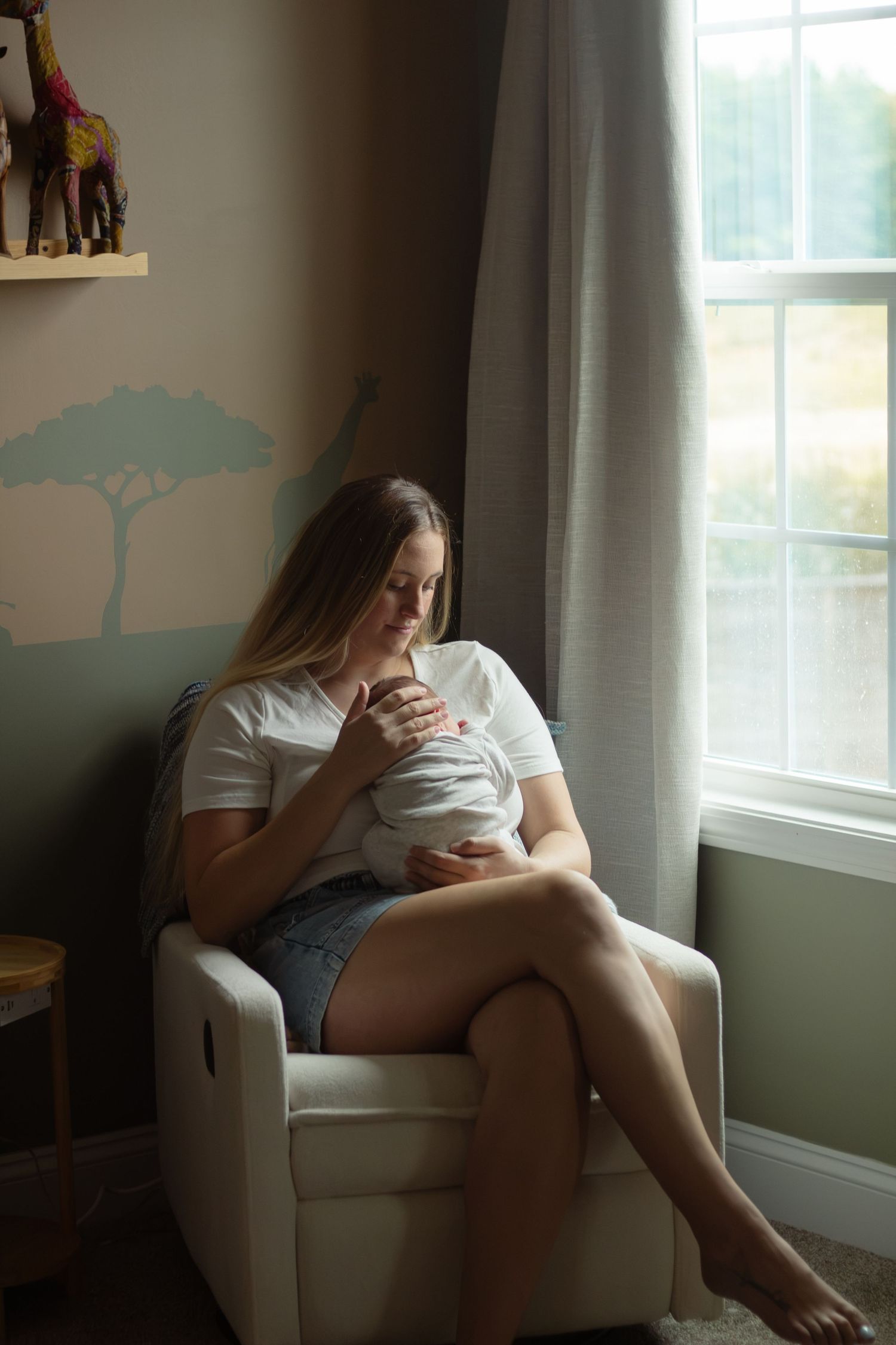 Mother holding newborn baby in arms in rocking chair in nursery during a newborn photography session in Fayetteville, NC.