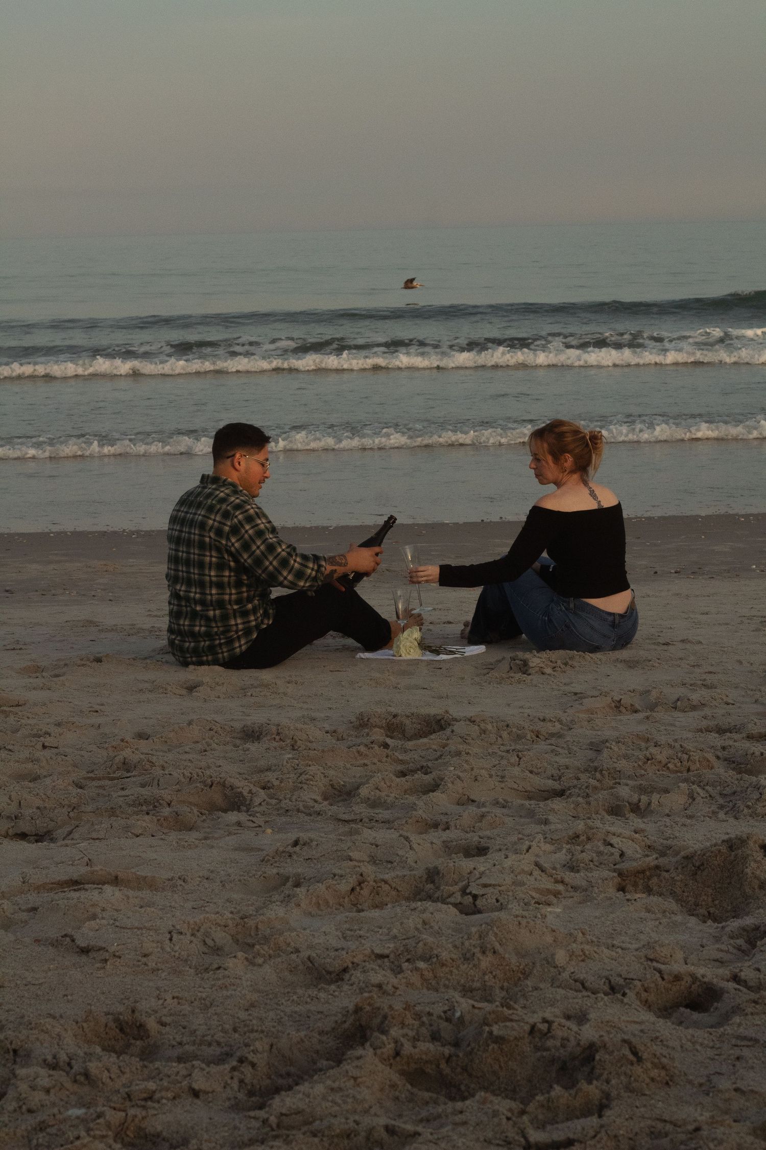 Couple sharing champagne by the water during a natural engagement photography session in Wrightsville Beach, NC.