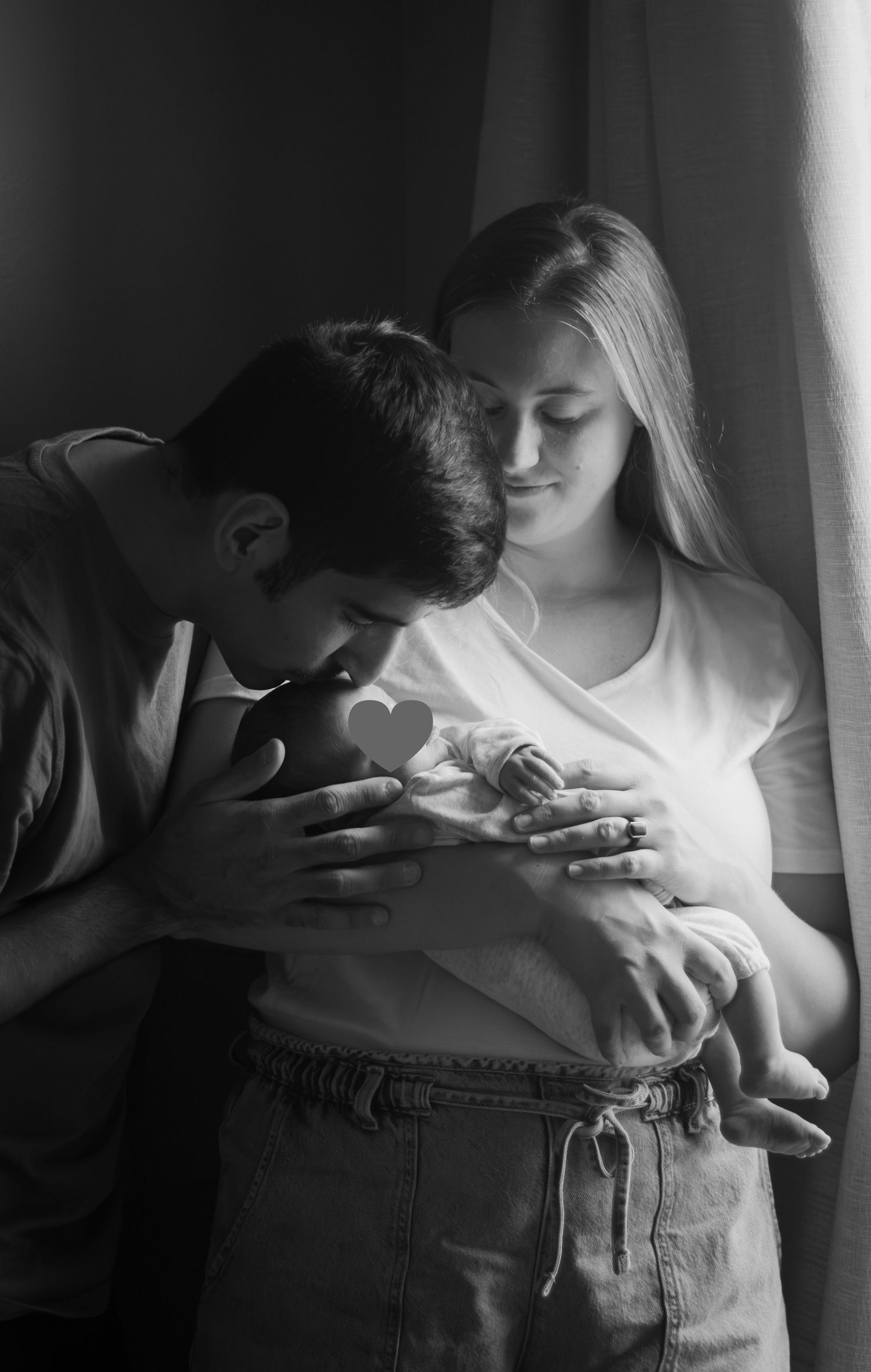 Parents gently holding their newborn baby and kissing forehead during a Fayetteville, NC newborn photography session.