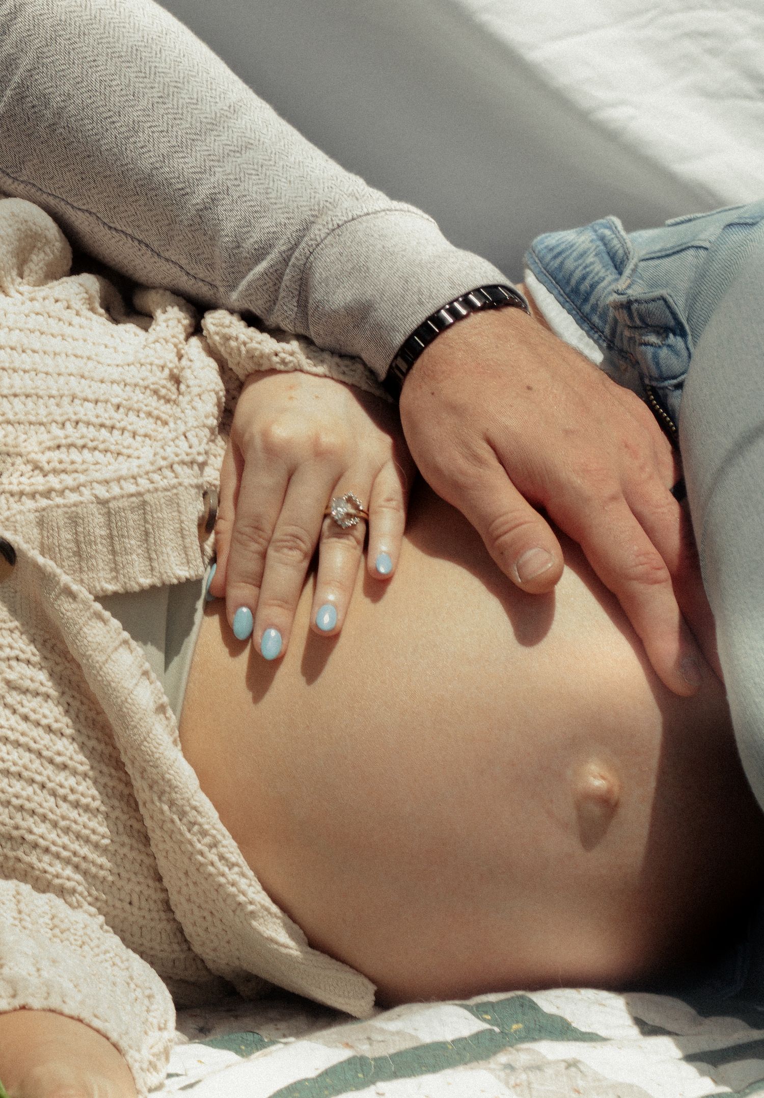 Close-up of mother's pregnant belly with father hand on it during a candid maternity photography session in Fayetteville, NC.