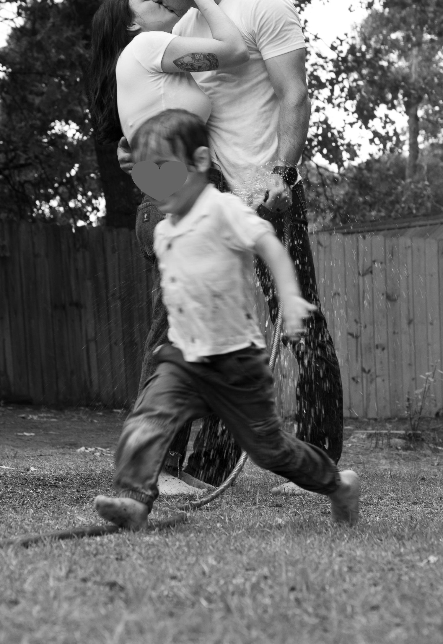 Family laughing and spraying each other with a garden hose during a playful family photography session in Raeford, NC.