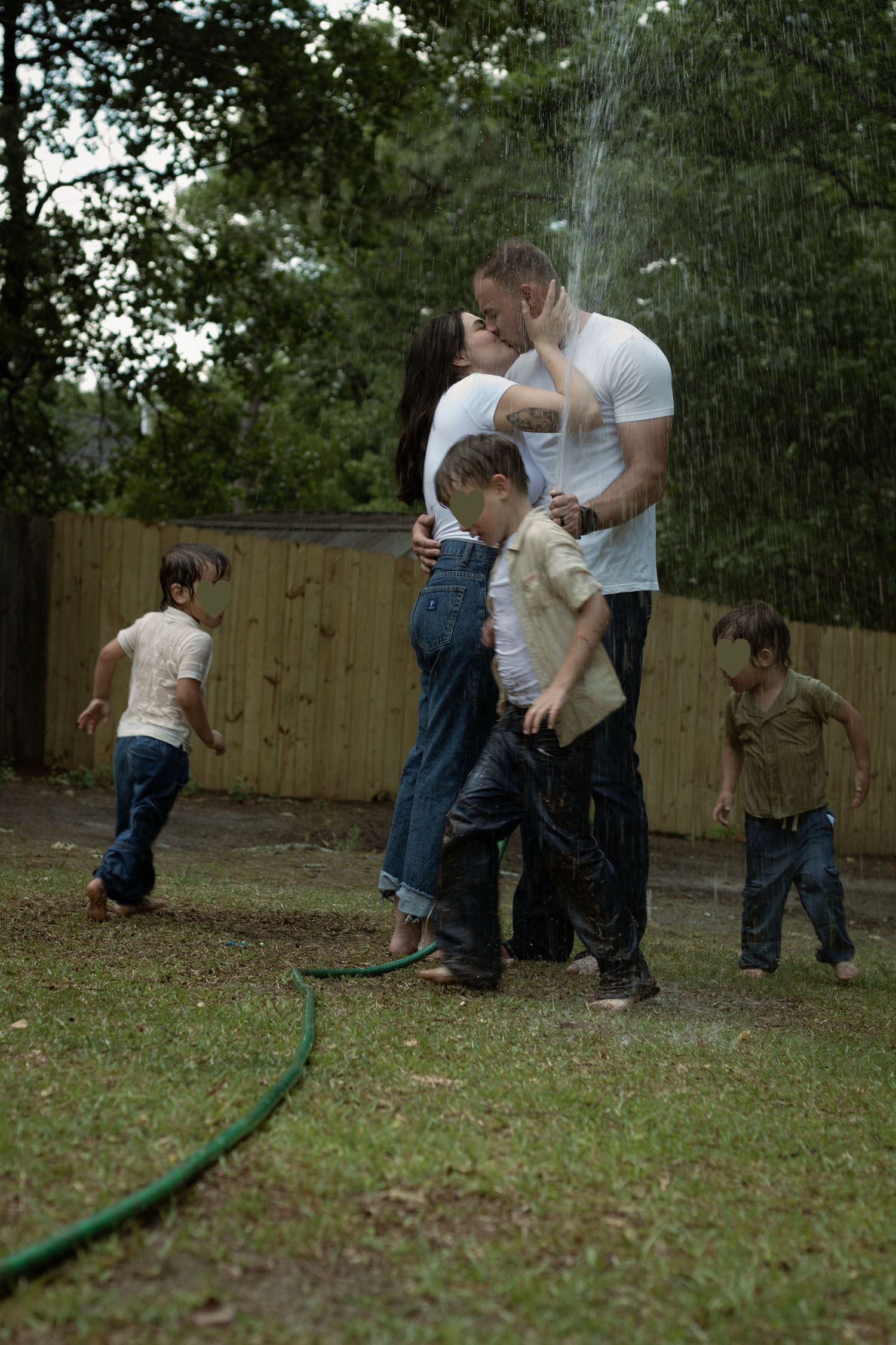 Family laughing and spraying each other with a garden hose during a playful family photography session in Raeford, NC.