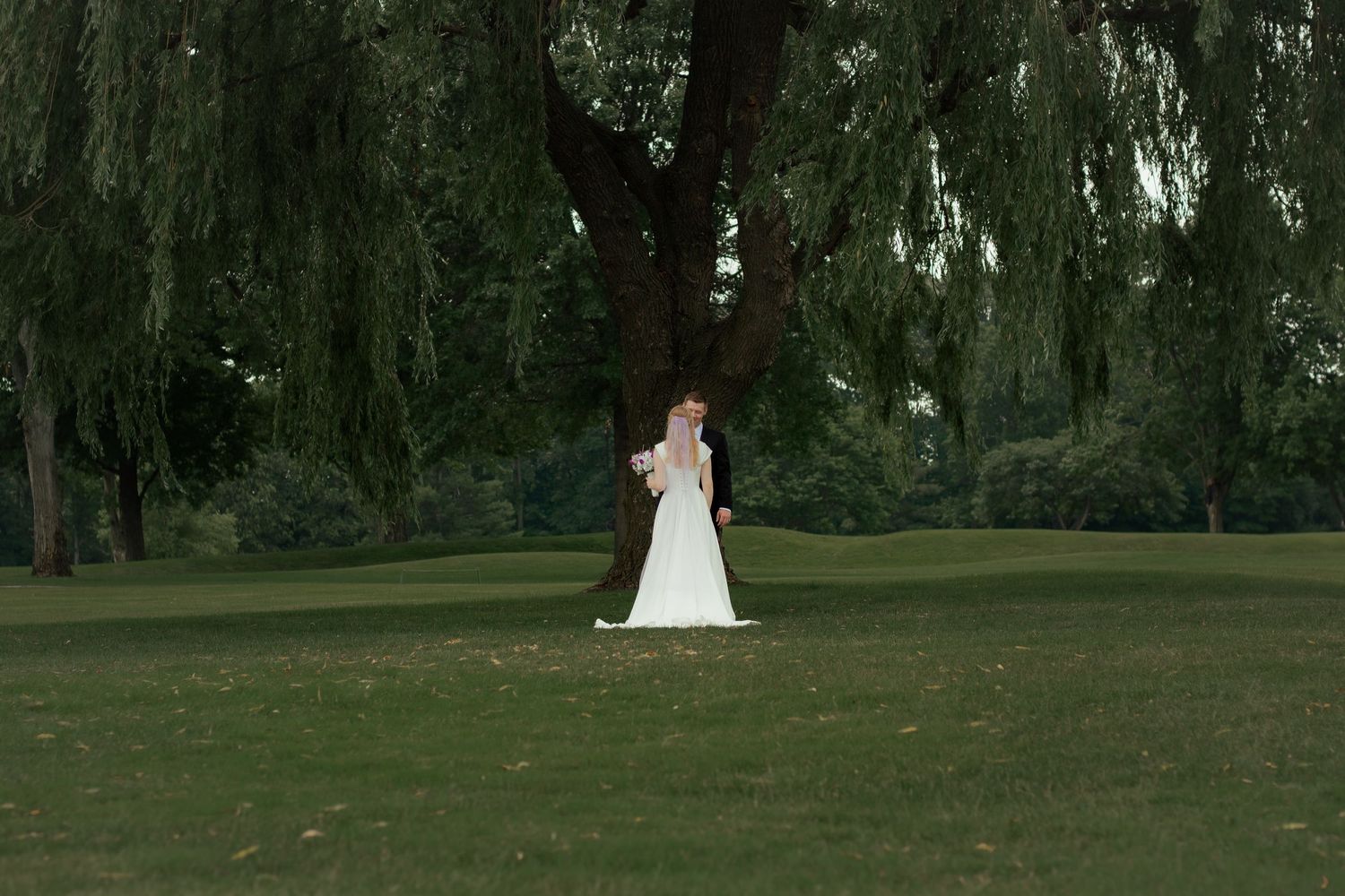 Bride and groom first look under giant willow tree on their wedding day in Lansing, Michigan.
