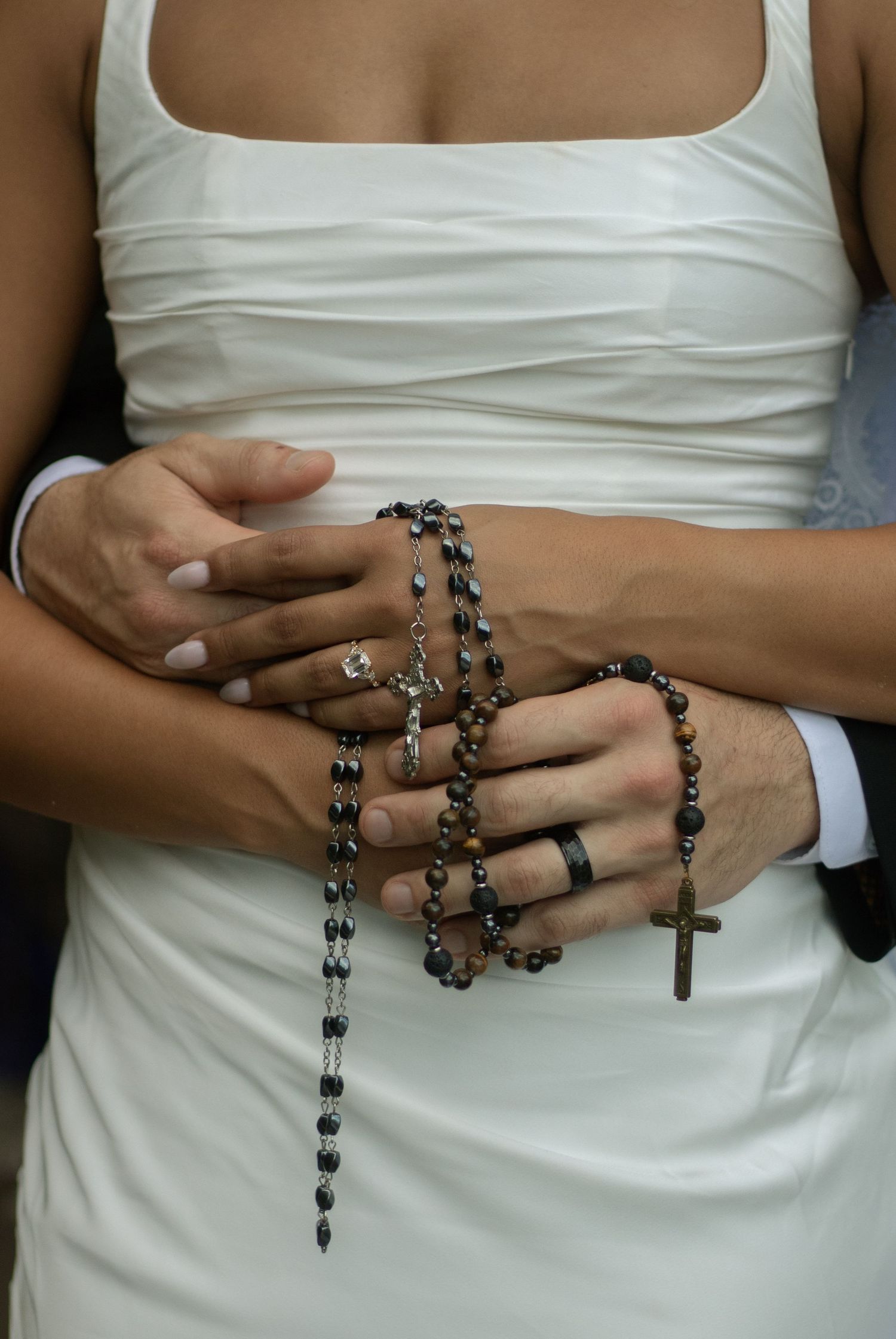 Close-up of bride and groom rosary beads entangled with hands showing wedding bands after their small church wedding in Fayetteville, NC.