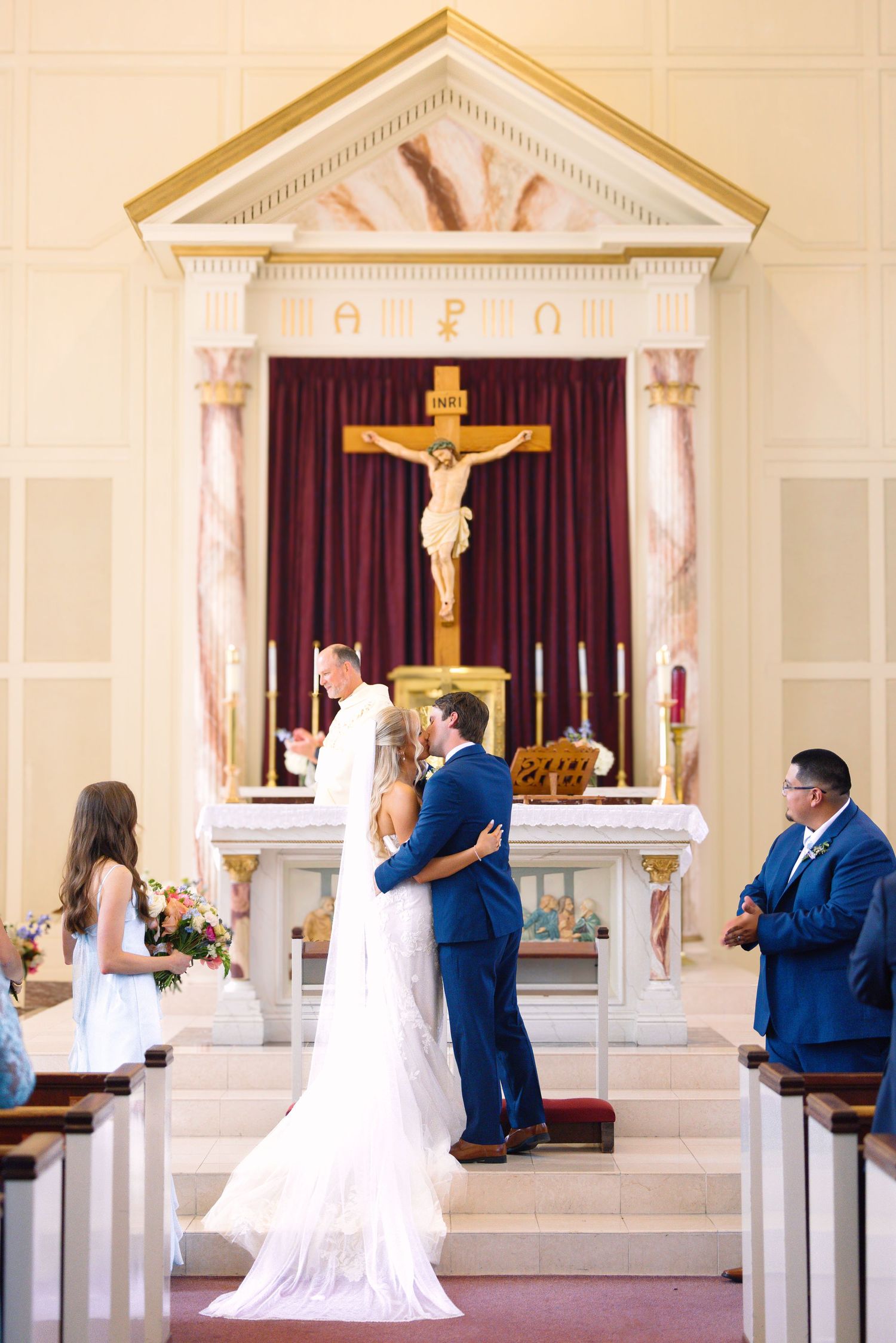 Bride and groom share first kiss at altar during Catholic church wedding ceremony.