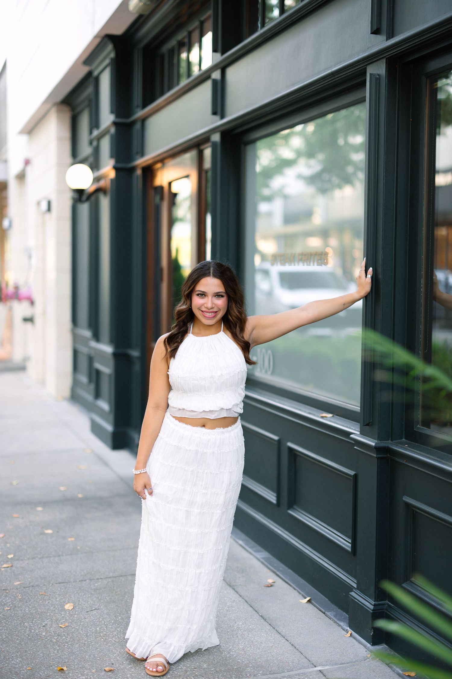 A sequence of five photos showing someone in a white dress posing playfully on a city sidewalk near dark storefronts.