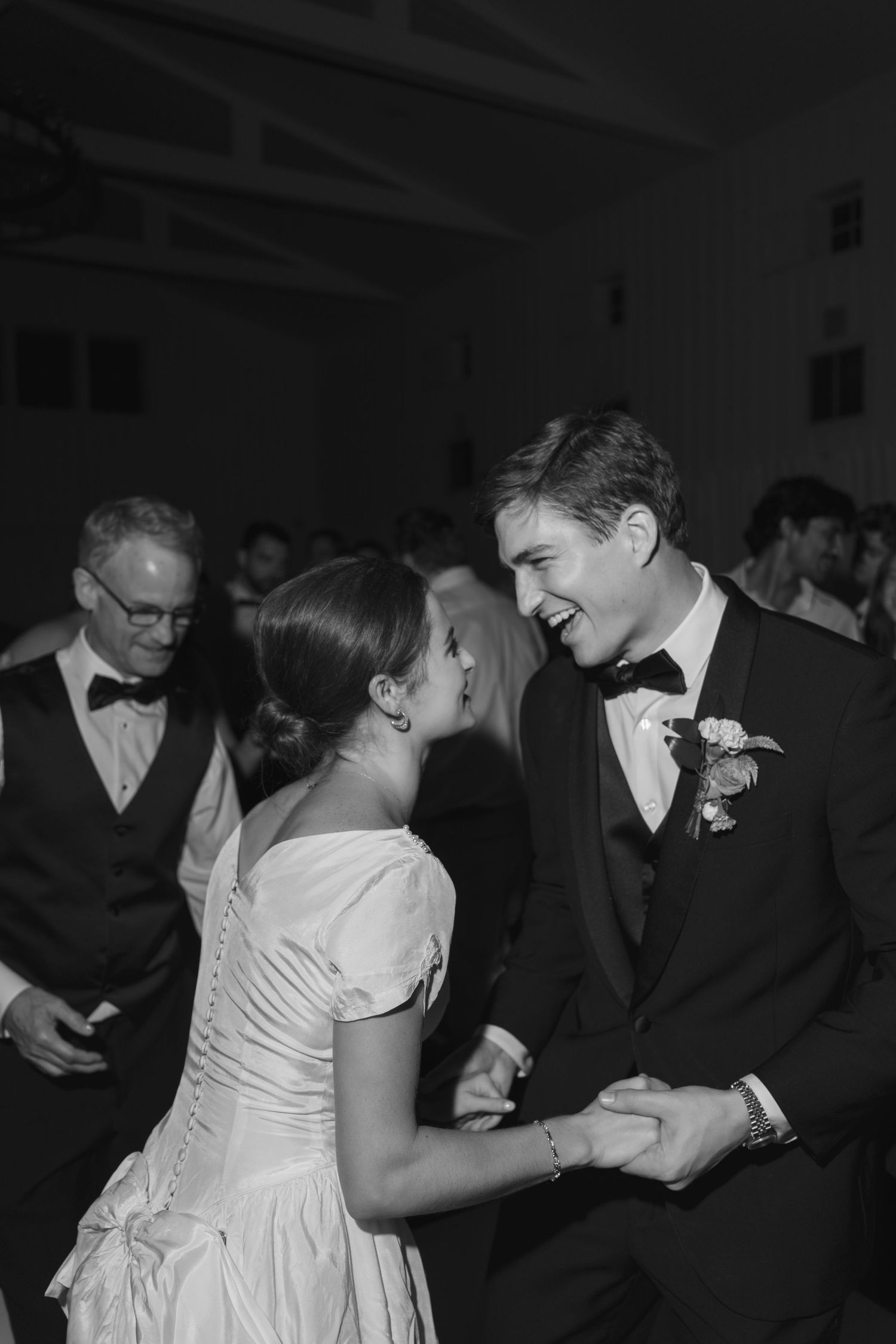 Black and white photo of a laughing bride and groom dancing together at their wedding reception.