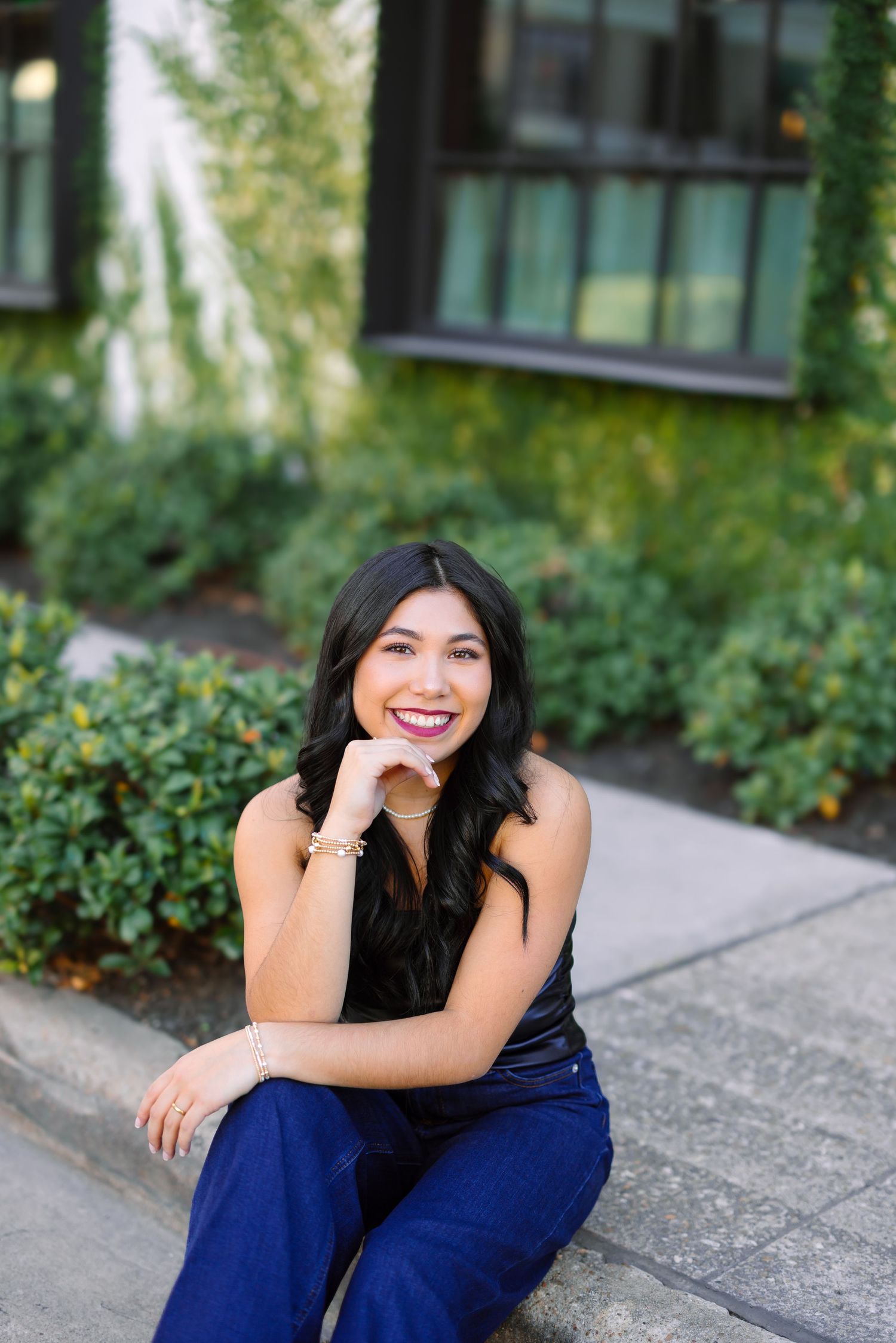 Woman in navy outfit sits casually outdoors against modern building background.