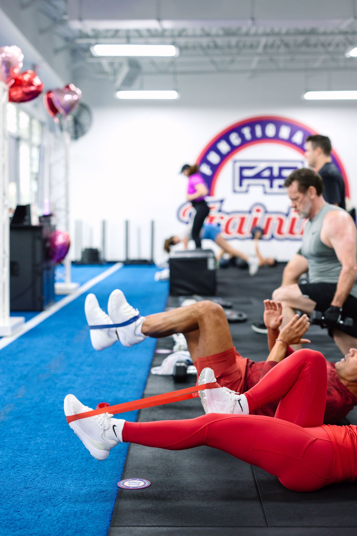 People exercising with resistance bands at F45 Training gym, wearing red workout gear on black floor mats.