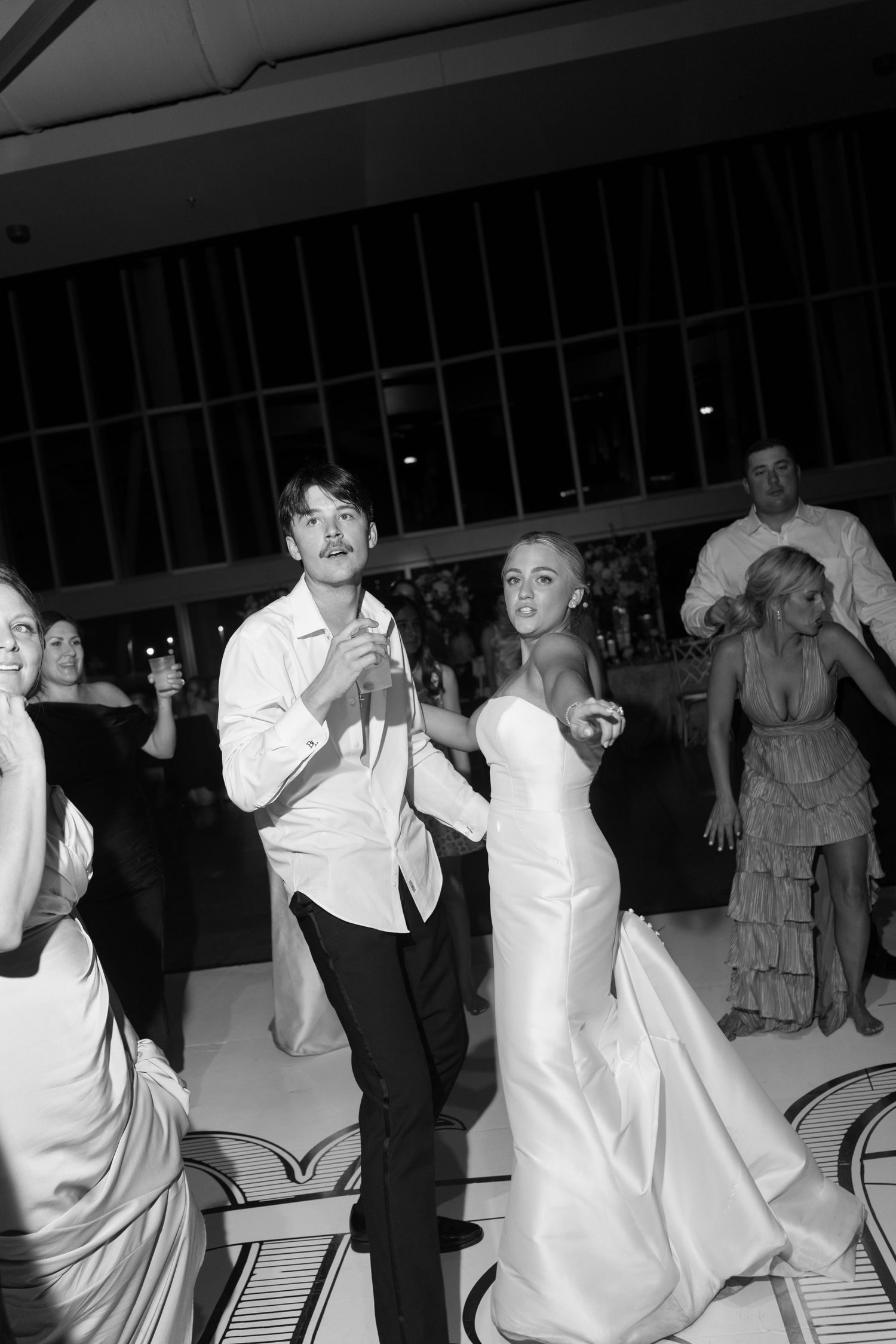Bride and groom dance joyfully with guests at their wedding reception in this classic black and white photo.