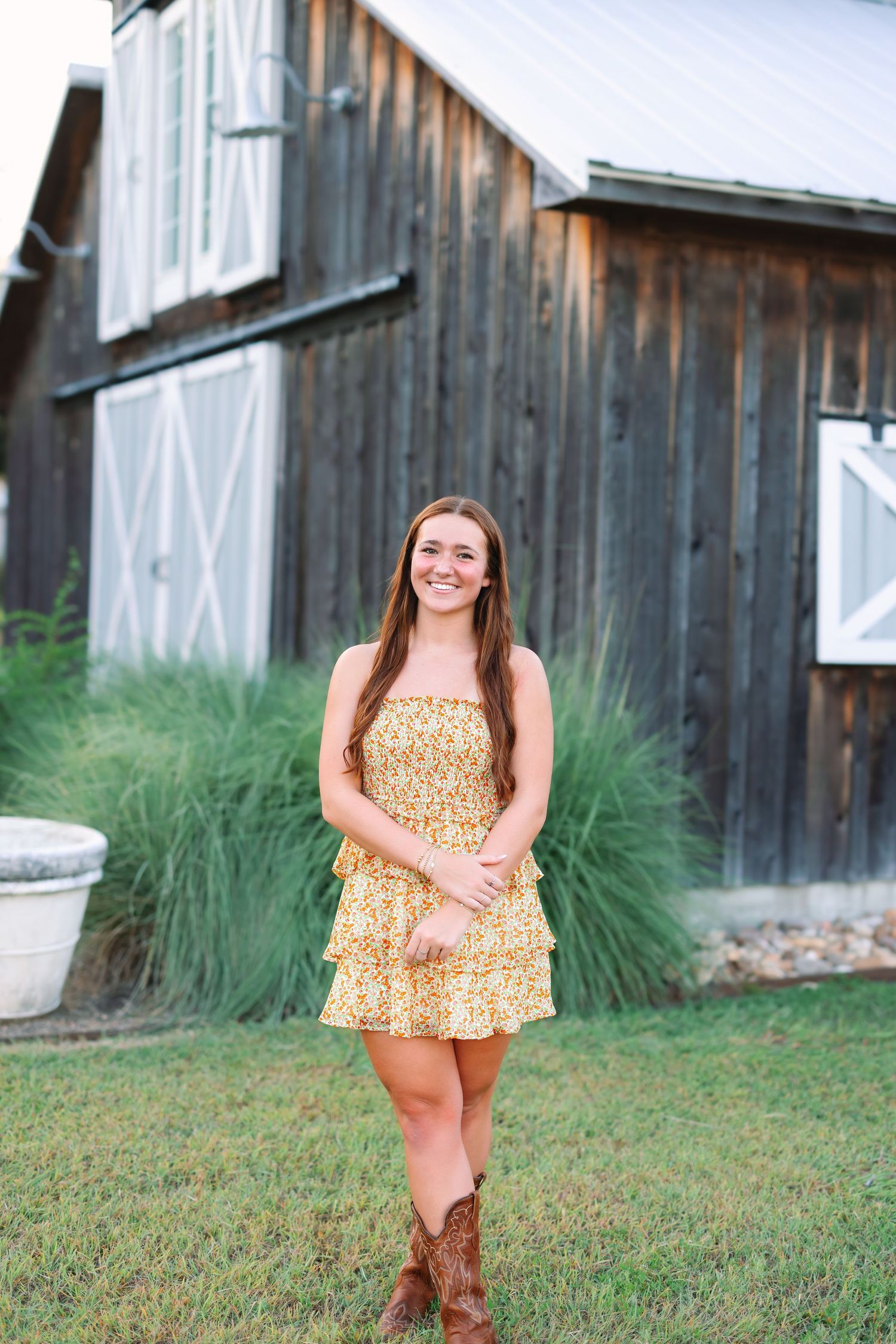 A yellow floral romper paired with brown boots is showcased against a rustic barn setting.