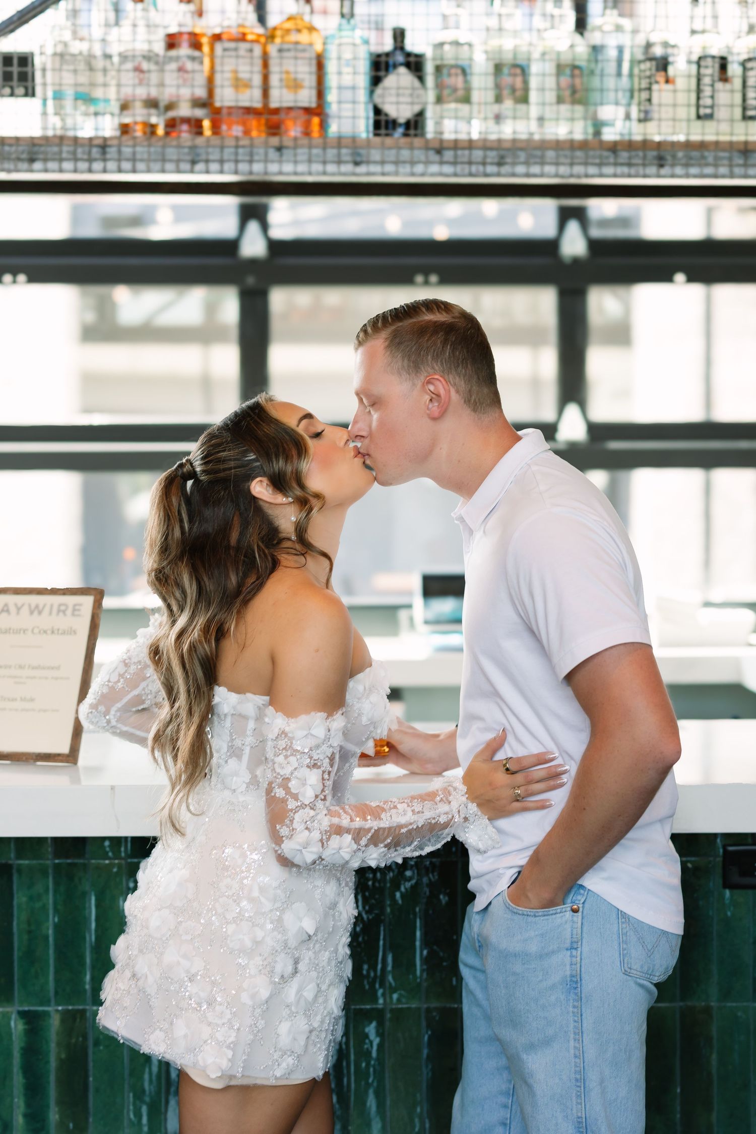 Couple sharing a romantic kiss at a bar, woman in white lace dress and man in white polo shirt.