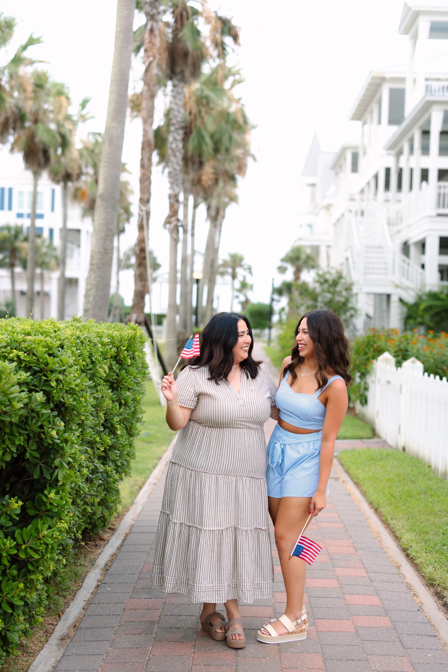 Friends walk and laugh together on a palm tree-lined pathway near beach houses.