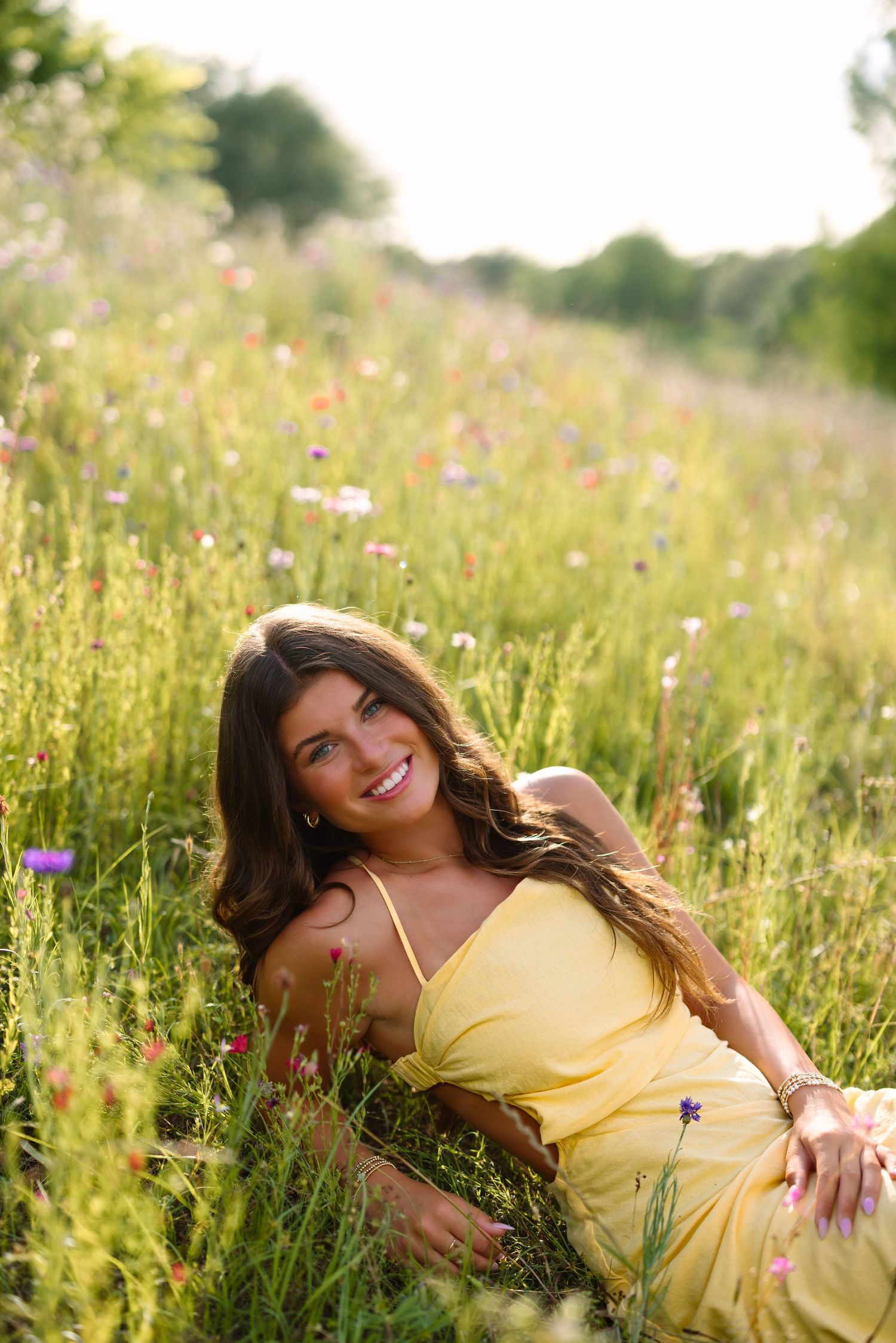 A person in a yellow dress lies among wildflowers in a sunny meadow.