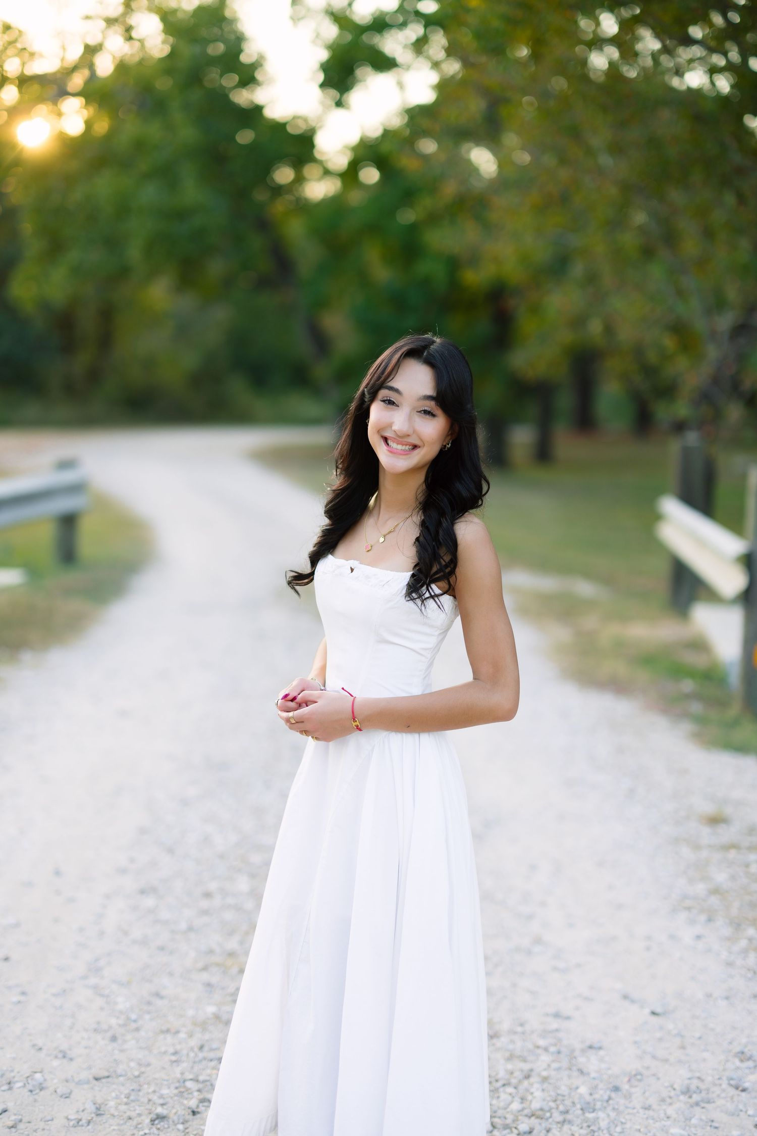 Joyful outdoor portraits in a flowing white dress on a gravel path.