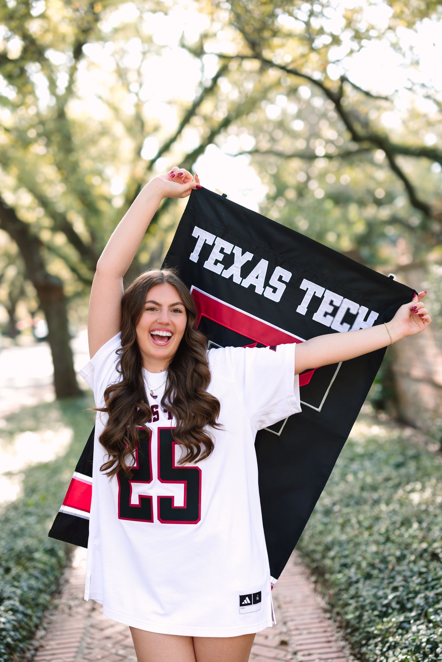 Excited graduate holding Texas Tech banner and wearing sports jersey outdoors.